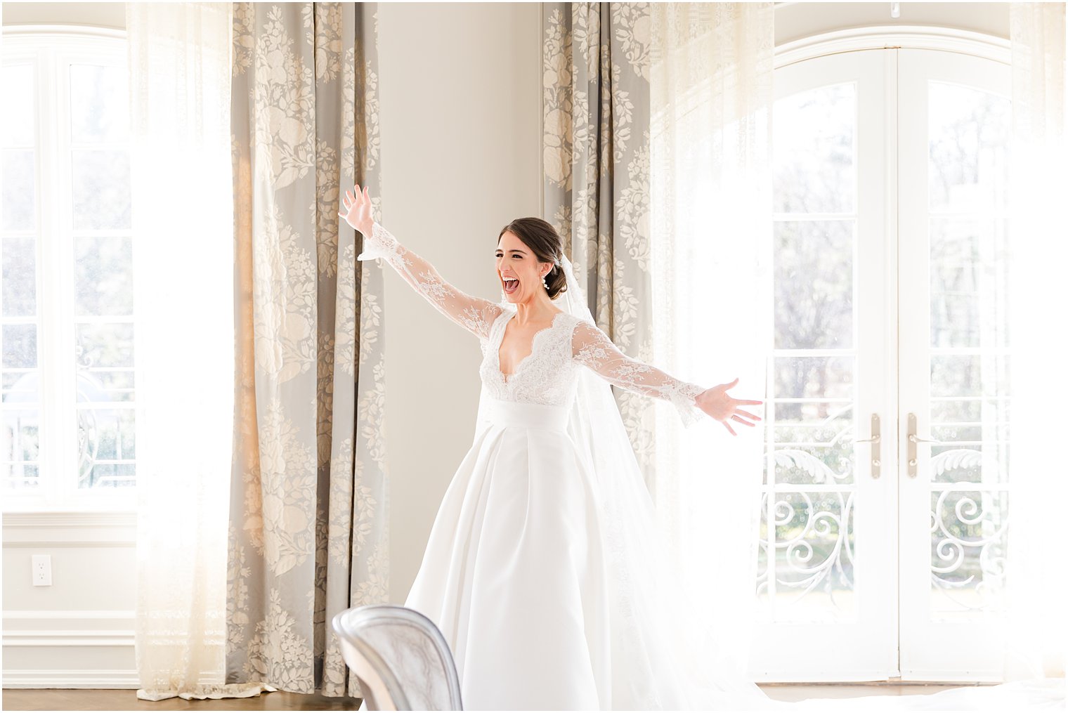 bride holds out arms for bridesmaids during first look