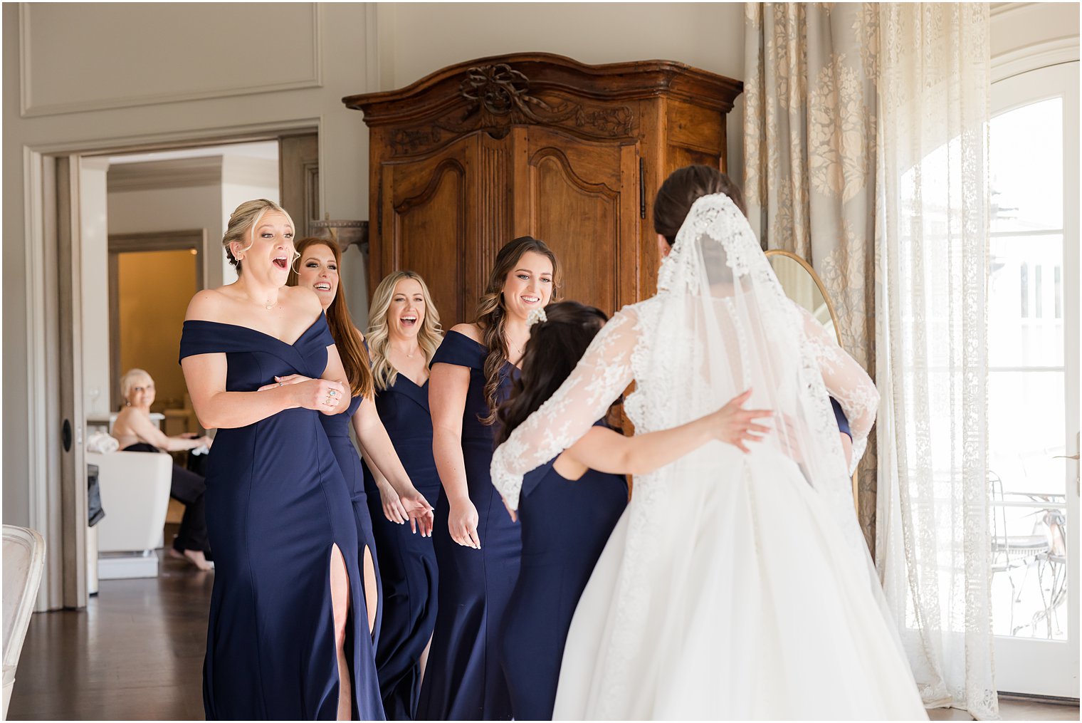 bridesmaids in navy gowns look at bride during first look 