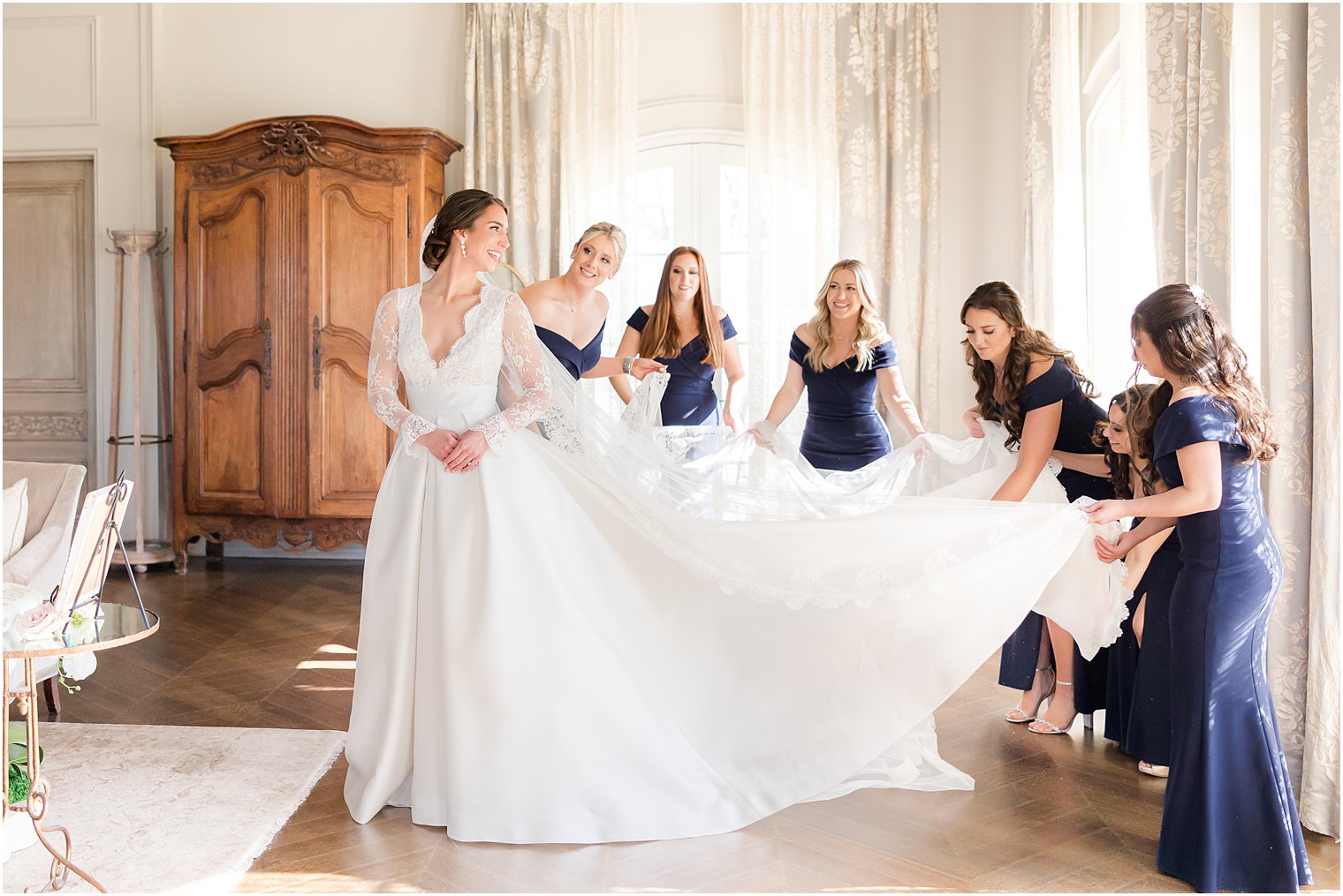 bridesmaids in blue dresses lay out bride's train and skirt 