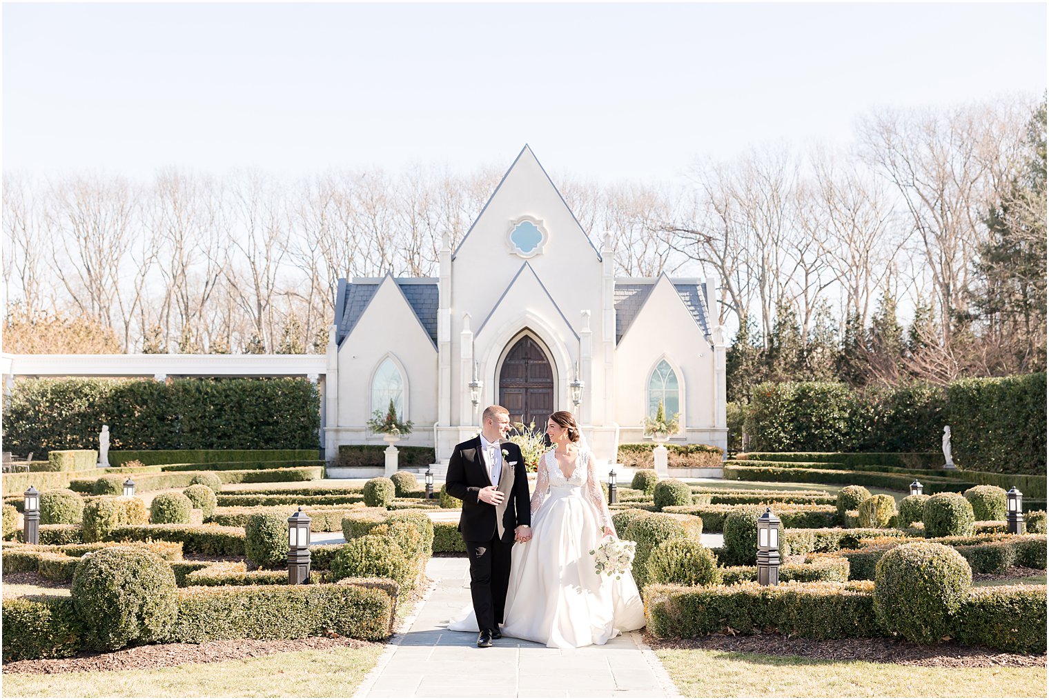bride and groom walk through gardens by chapel at Park Chateau Estate