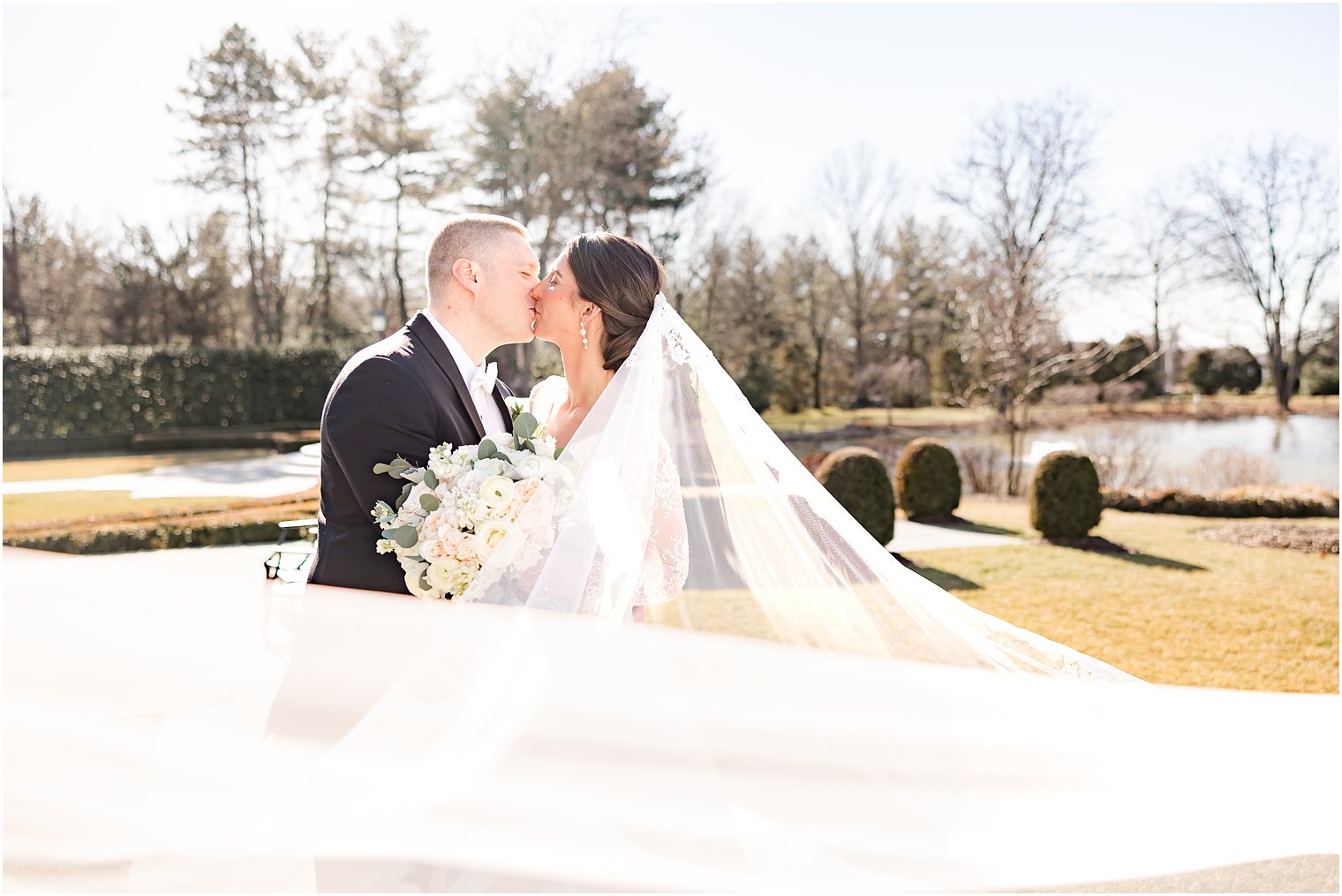 bride and groom kiss with bride's veil wrapped around them 