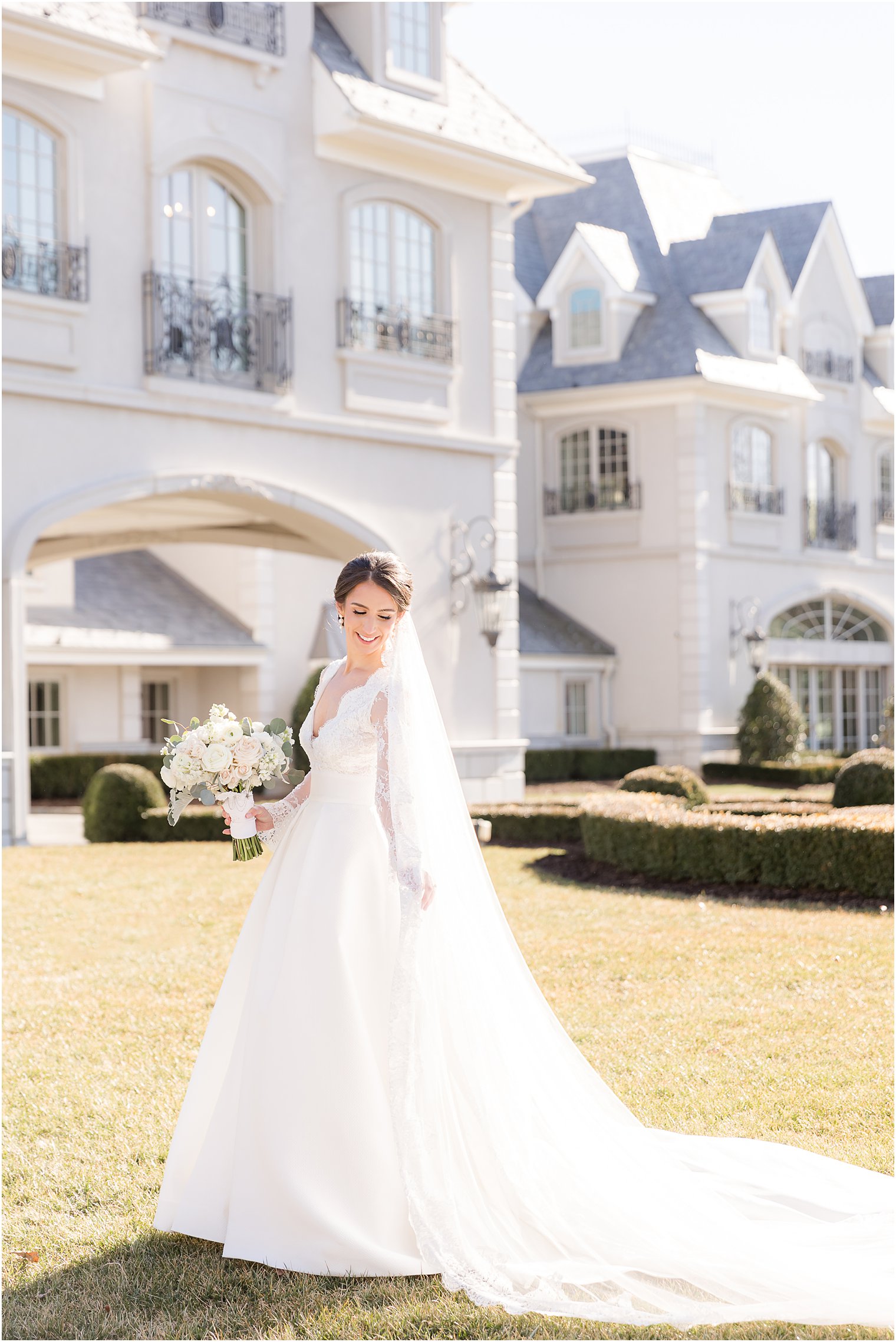 winter bride in wedding gown with lace sleeves moves skirt of wedding gown on lawn at Park Chateau Estate