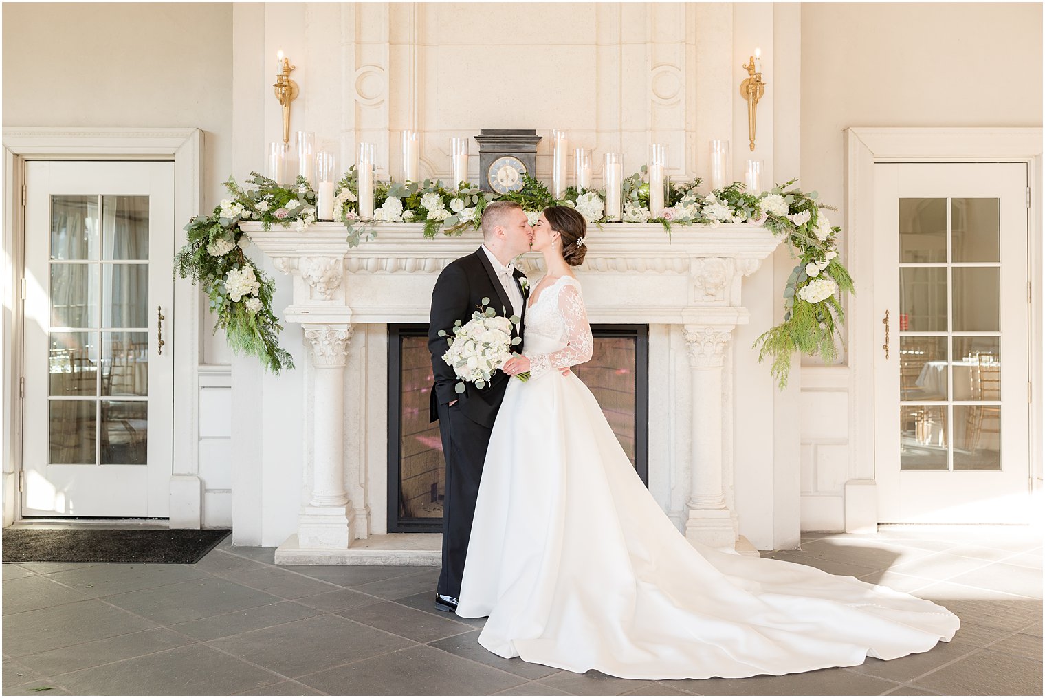 newlyweds kiss by fireplace with greenery draped across top