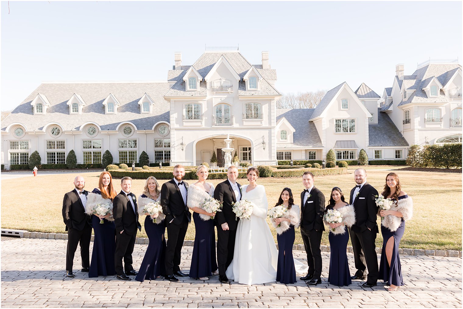bride and groom pose with wedding party in navy dresses and black suits outside Park Chateau Estate