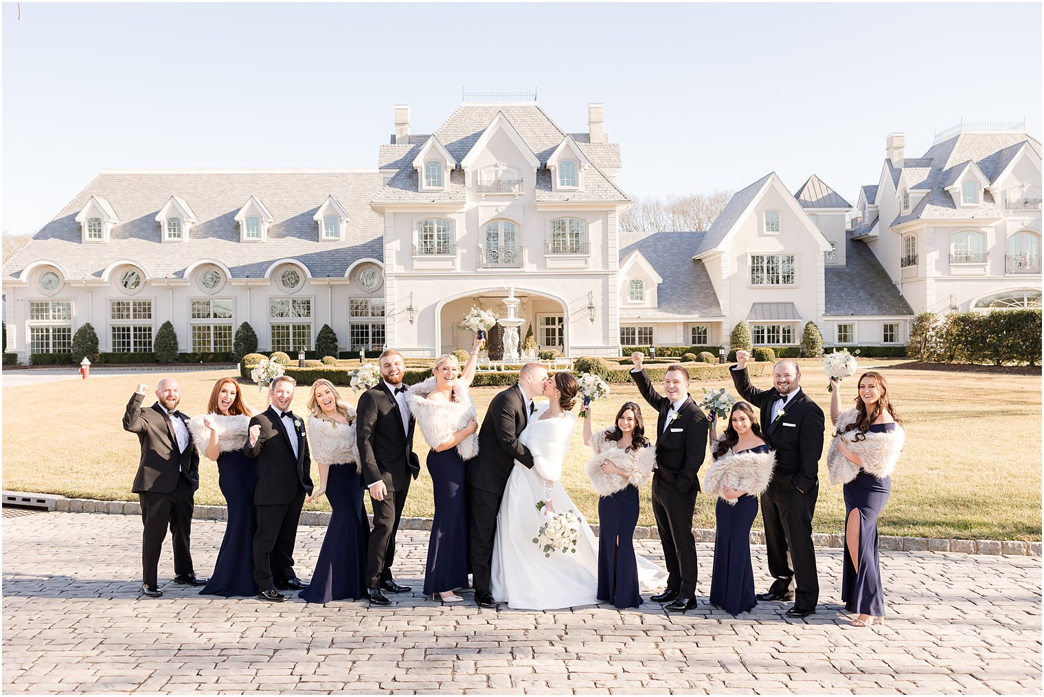 newlyweds kiss while wedding party cheers in front of Park Chateau Estate