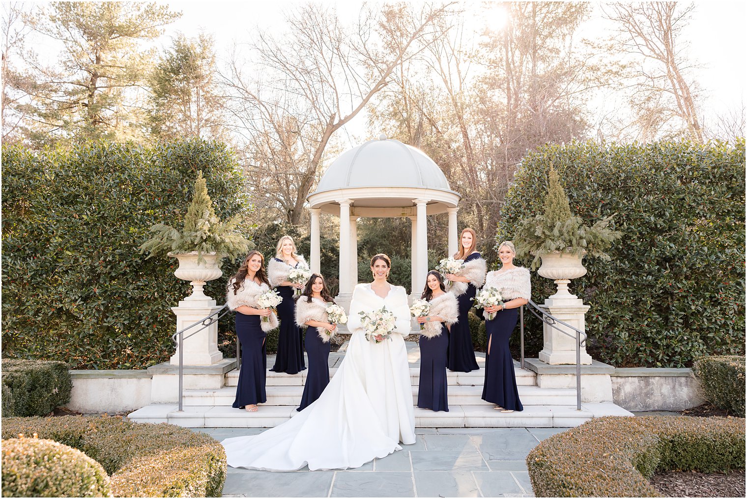 bride stands with bridesmaids in blue dresses with furs by gazebo at Park Chateau Estate