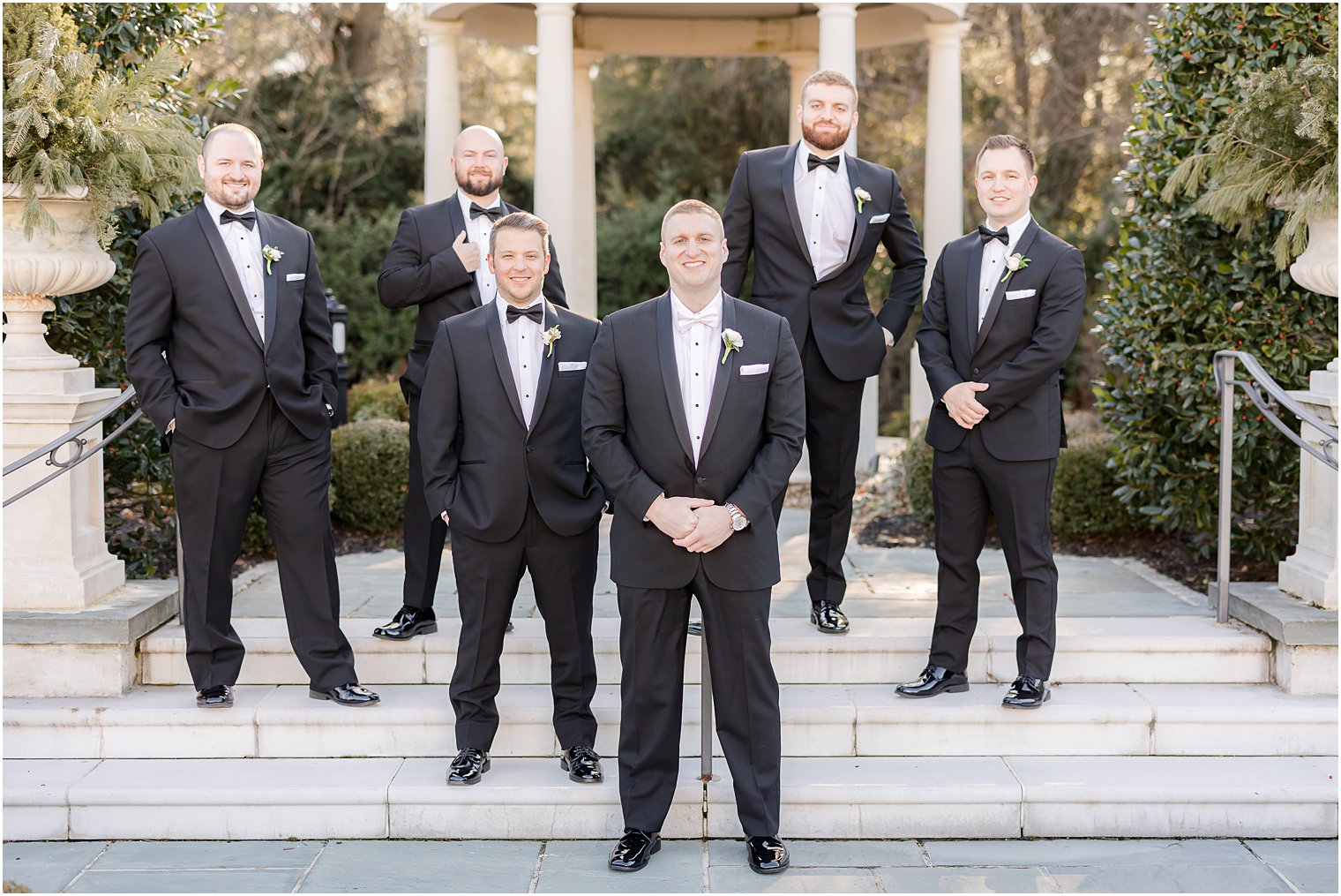 groom stands with groomsmen on steps of gazebo 