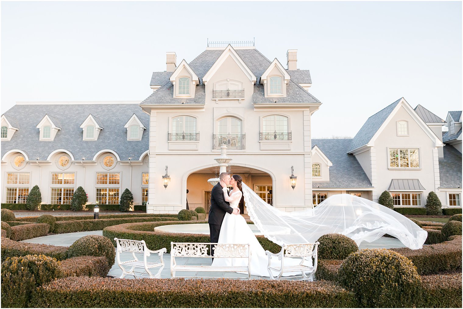 bride and groom hug on patio outside Park Chateau Estate with bride's veil floating 