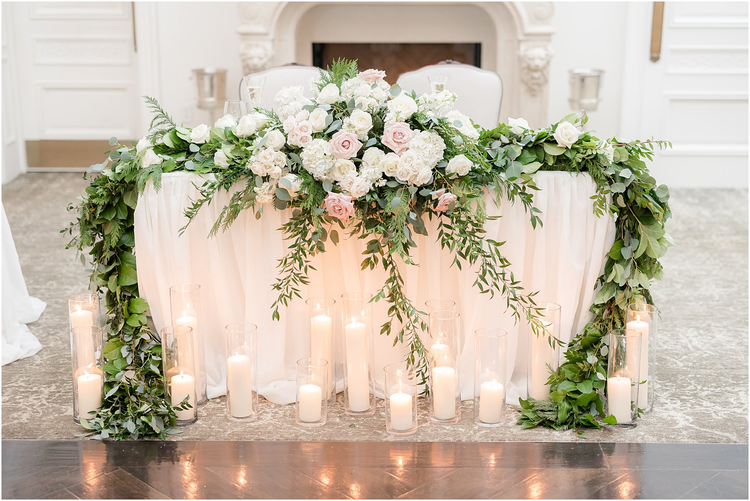 sweetheart table with candles in front and greenery draped around top 