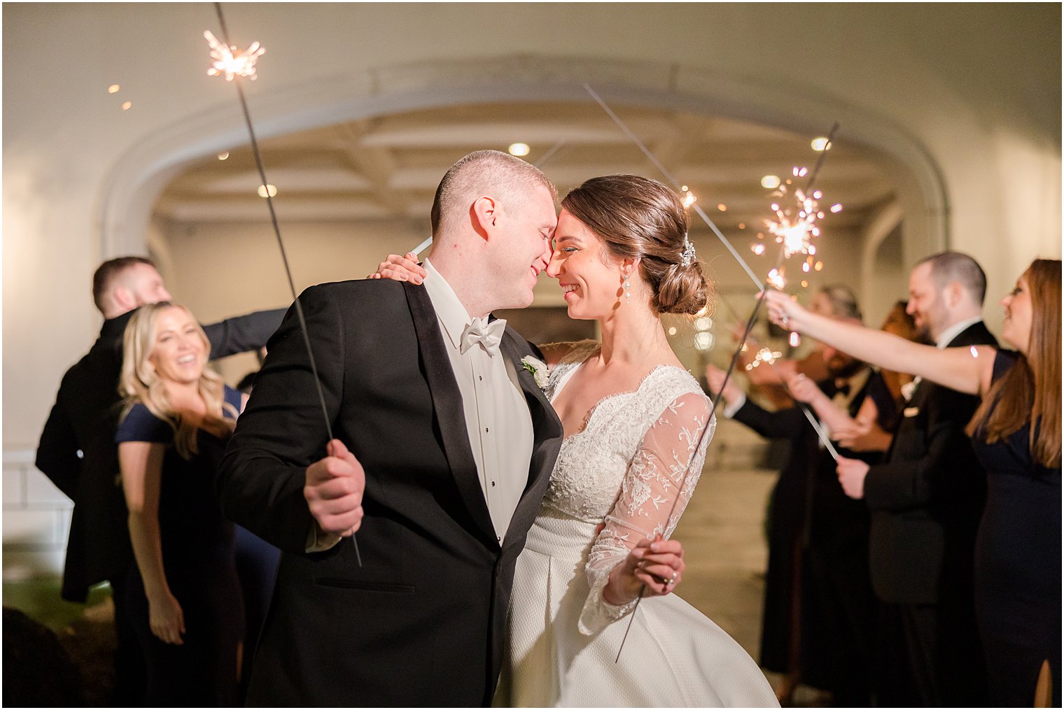 newlyweds lean heads together with sparklers behind them 