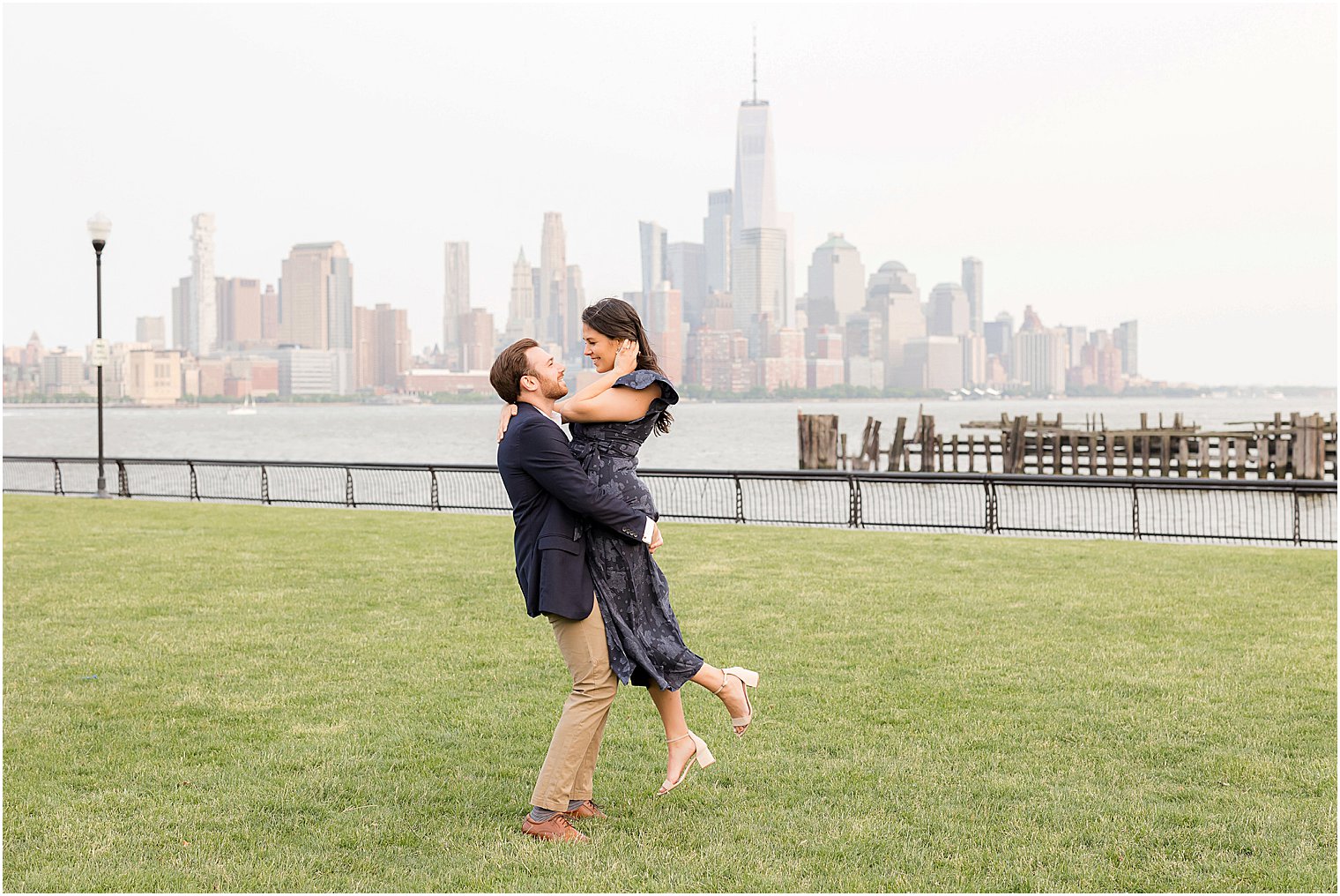 woman lifts man off ground in park during Hoboken engagement session