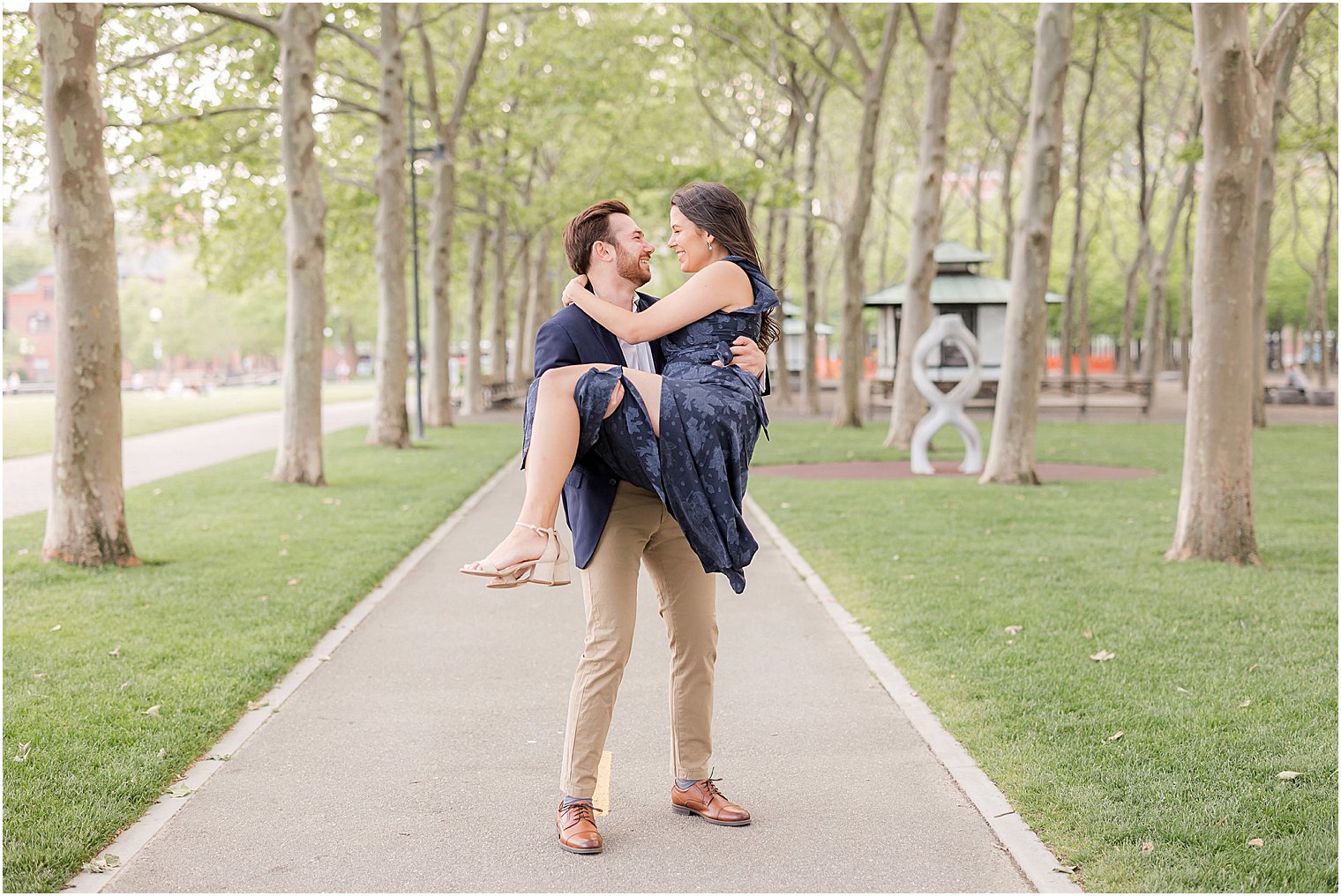man lifts woman on park pathway during Hoboken engagement session