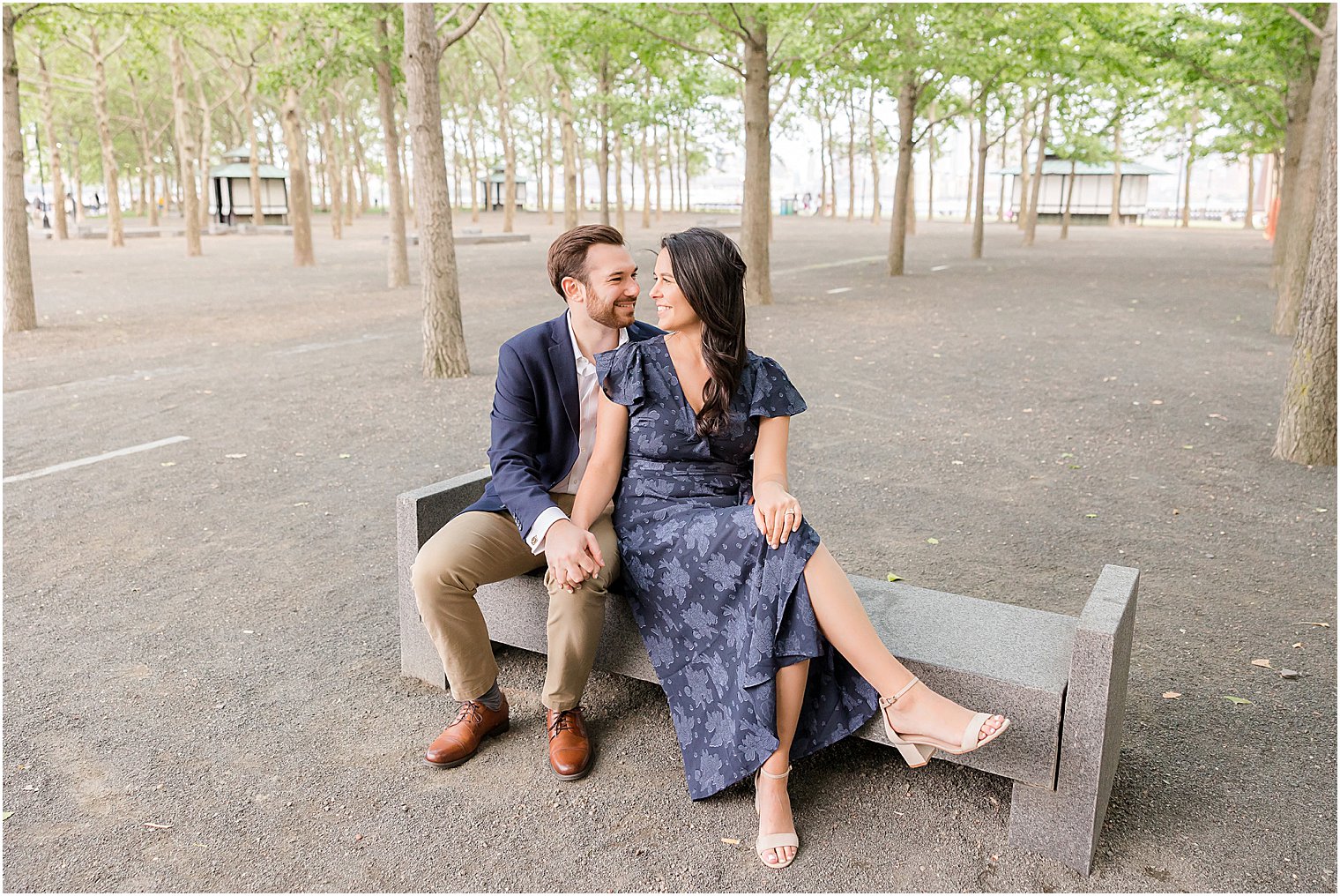 engaged couple sits on bench in park during Hoboken engagement session
