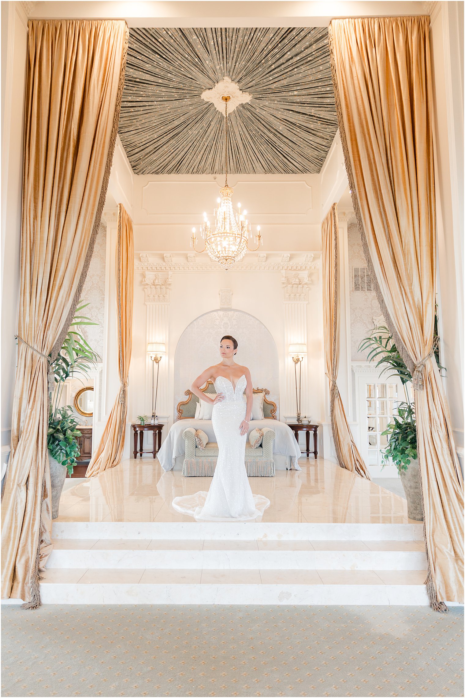 bride stands at foot of bed in suite at Mallard Island Yacht Club with hands on hip