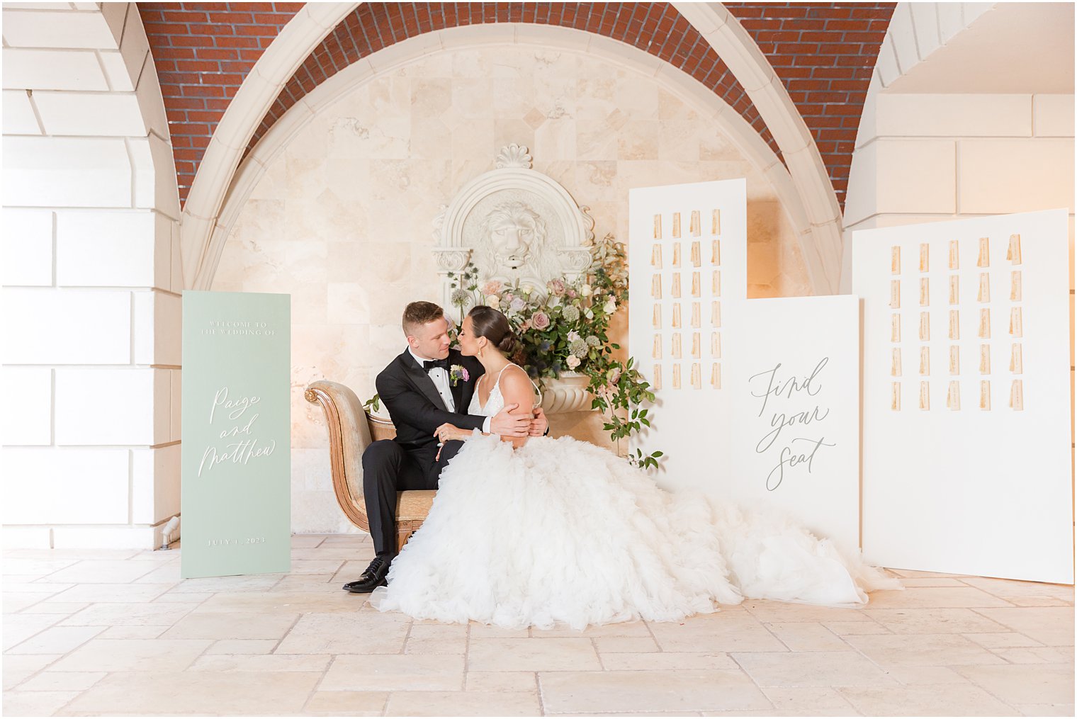 bride and groom sit leaning together on bench near seating chart at Mallard Island Yacht Club