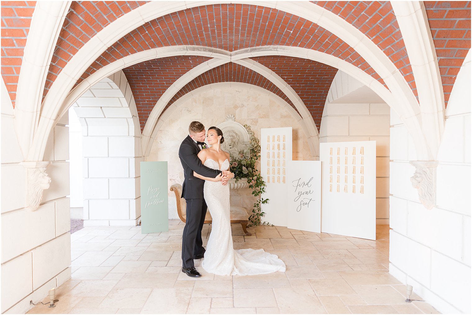 groom hugs bride from behind between modern seating chart signs and seating area at Mallard Island Yacht Club