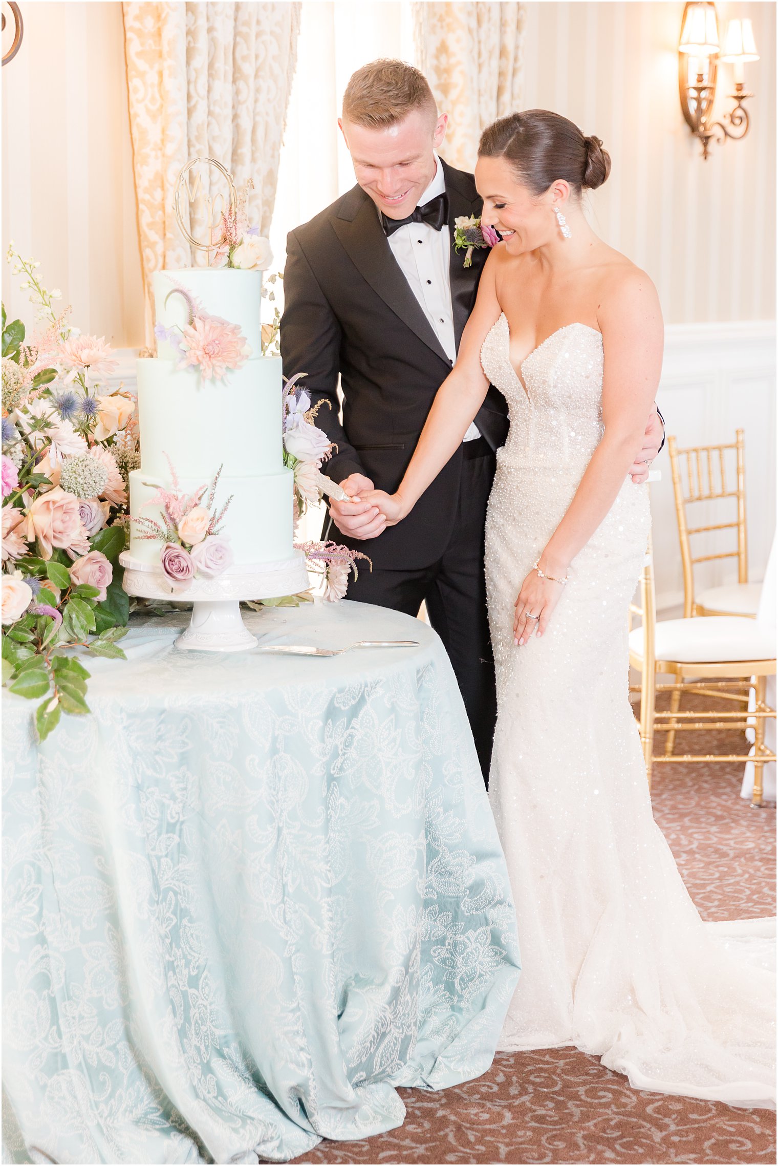 newlyweds cut tiered wedding cake sitting on blue table cloth at Mallard Island Yacht Club