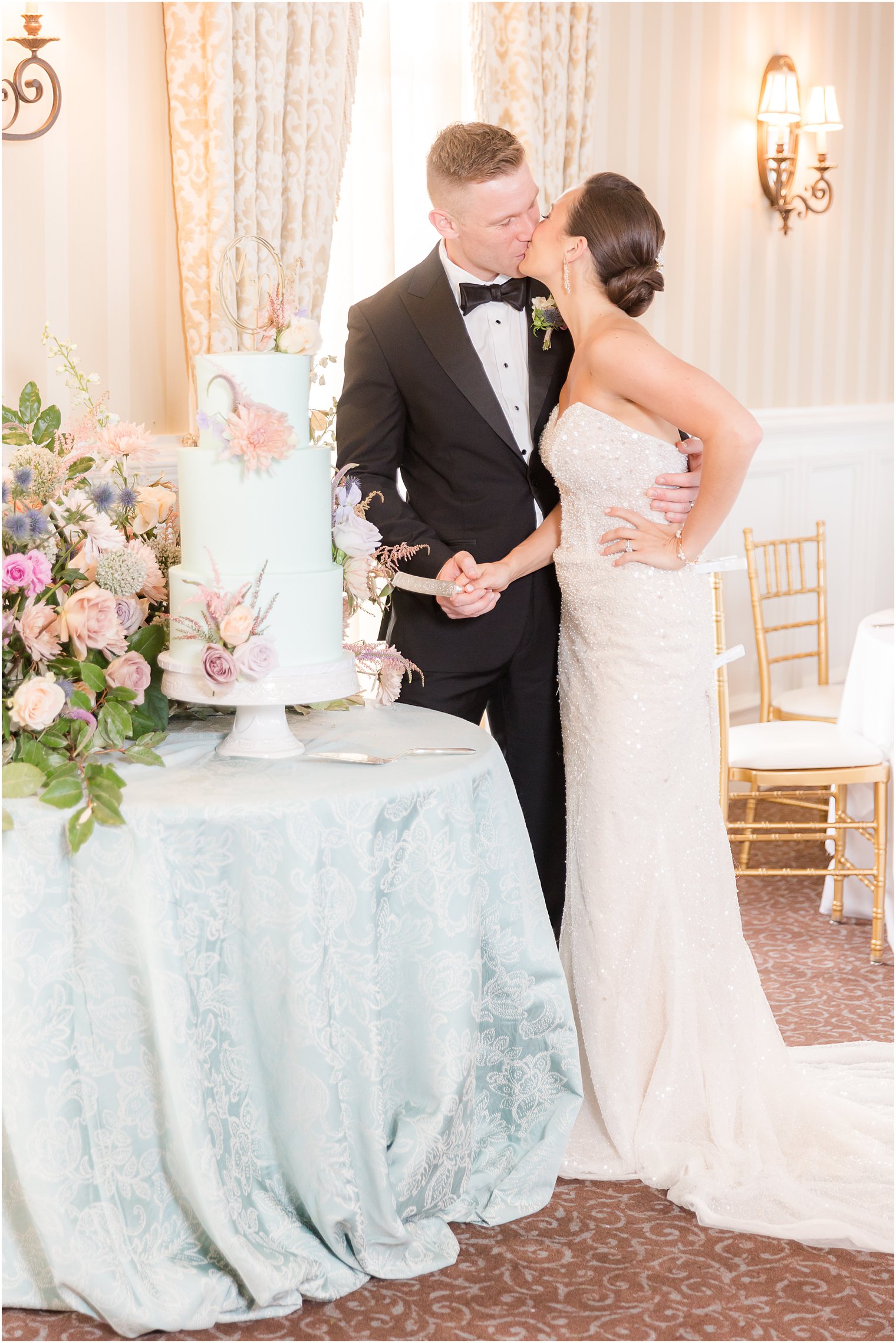 newlyweds cut tiered wedding cake sitting on blue table cloth at Mallard Island Yacht Club