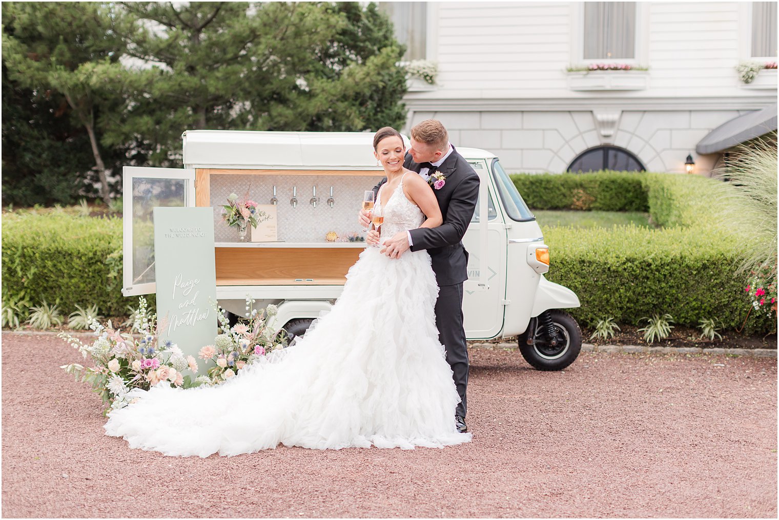 groom hugs bride from behind kissing her neck near mobile bar