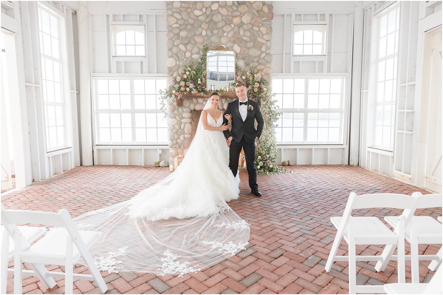 newlyweds stand by stone fireplace in barn at Mallard Island Yacht Club