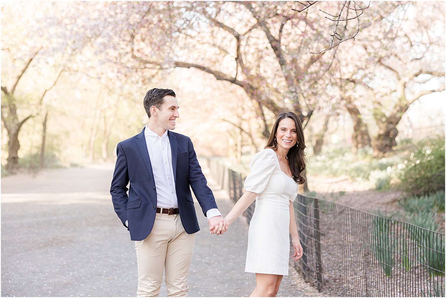 couple holds hands laughing walking through park during New York City engagement session