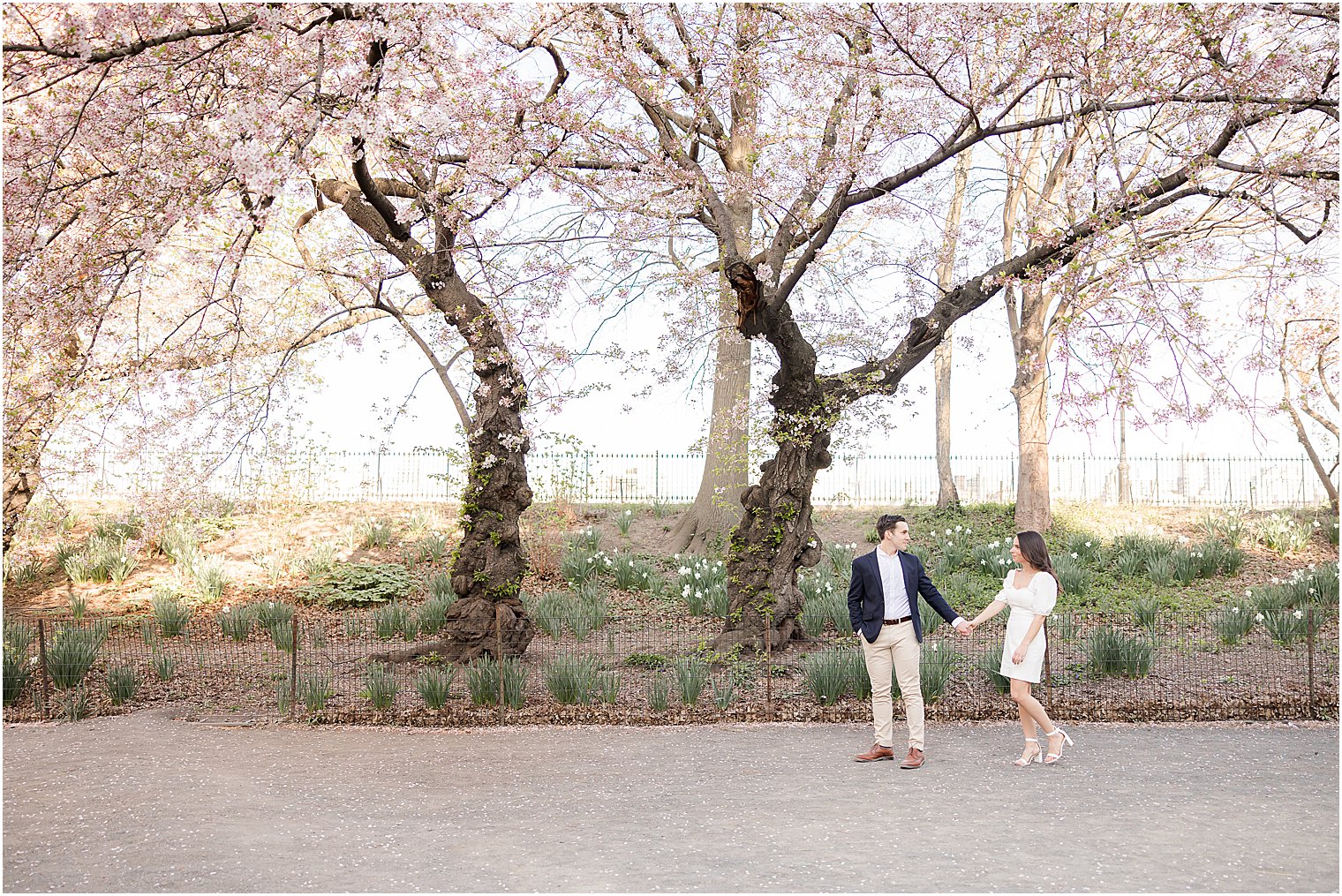 engaged couple holds hands walking down path in NYC park