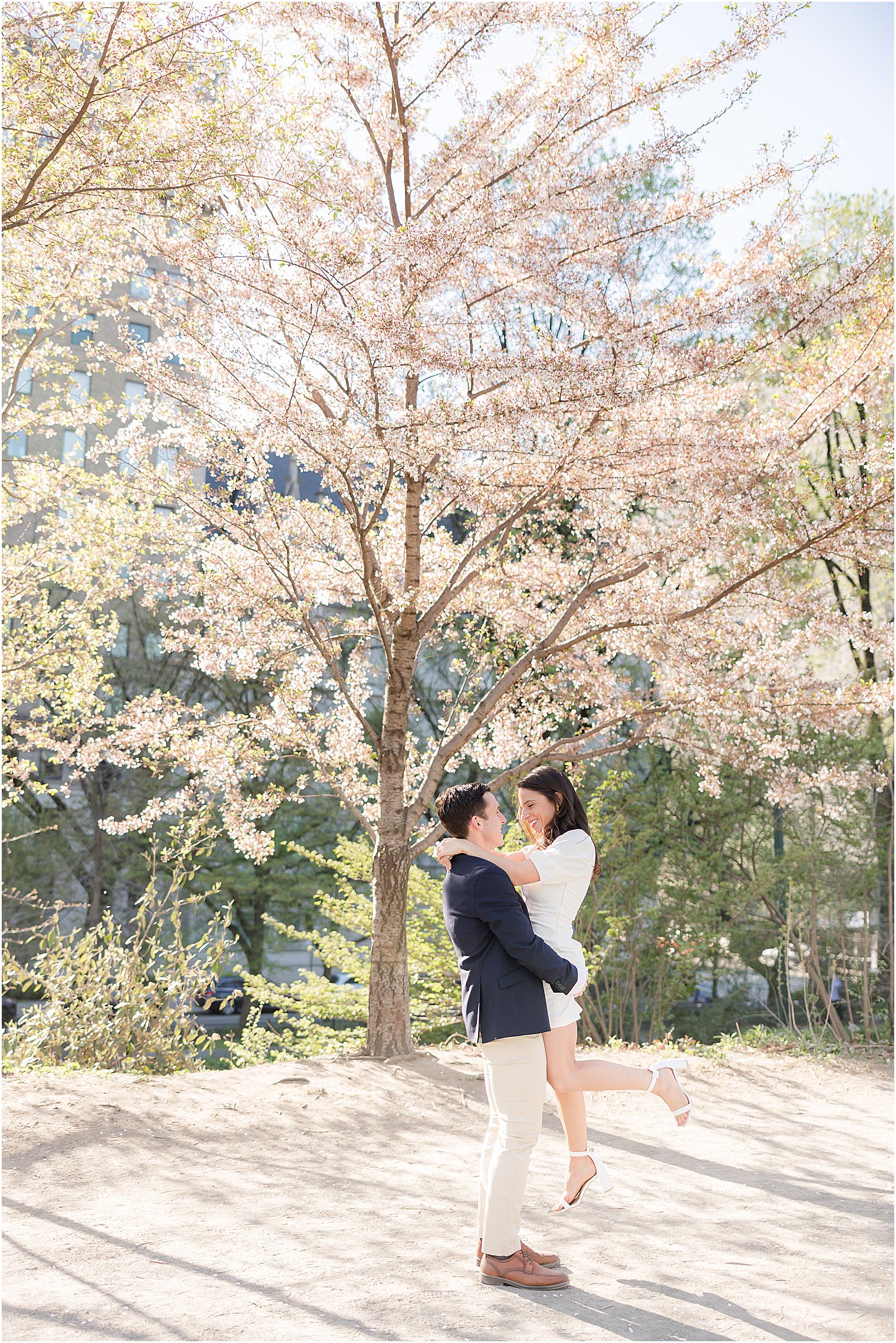 groom lifts bride in white dress during spring New York City engagement session