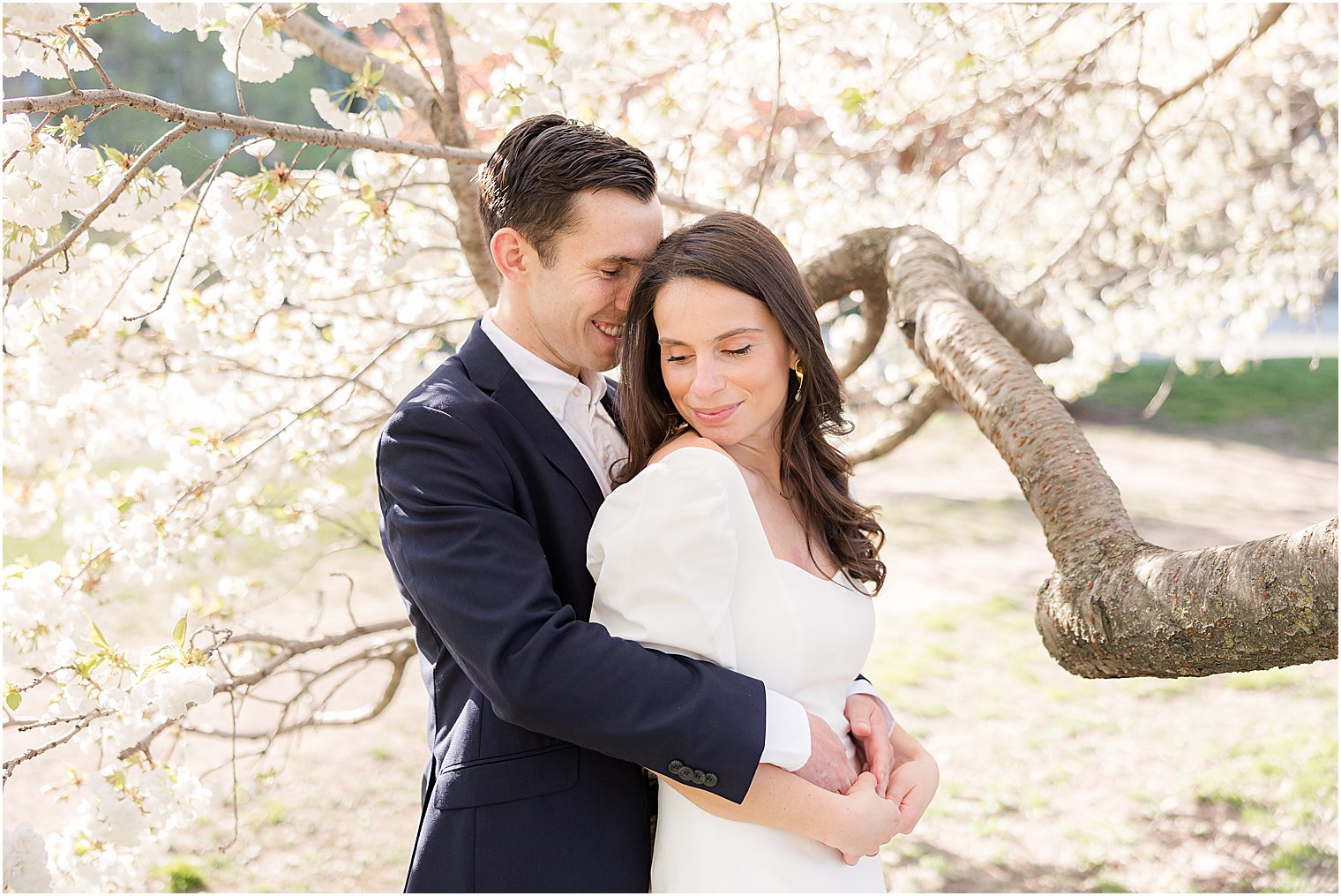groom in navy blazer hugs bride from behind during spring time New York City engagement session