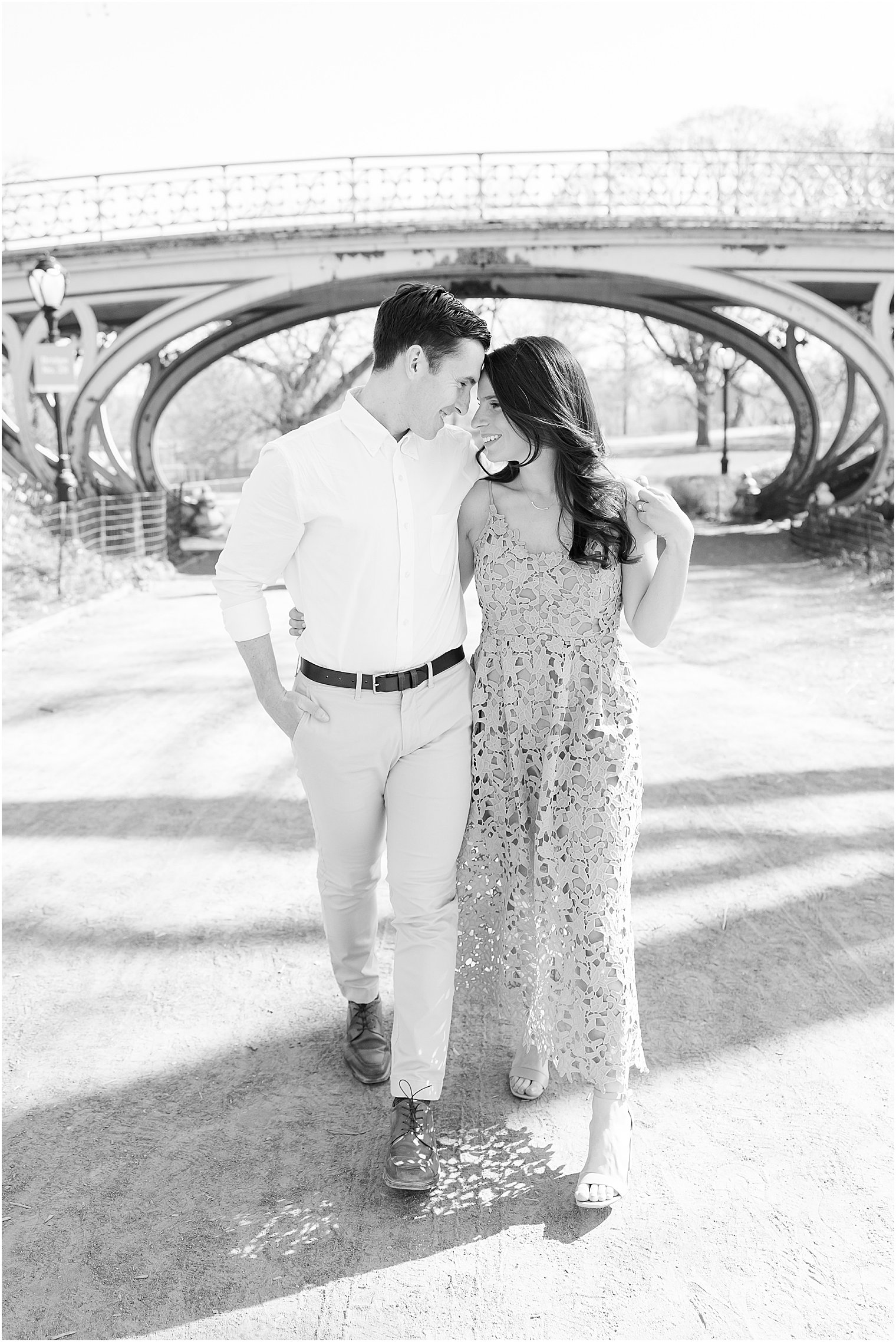 engaged couple walks leaning heads together near bridge in Central Park