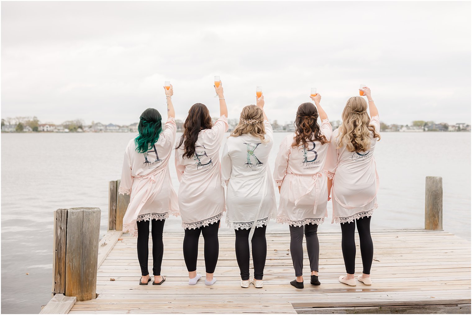 bridesmaids toast with champagne on dock in custom robes at Point Pleasant NJ airbnb