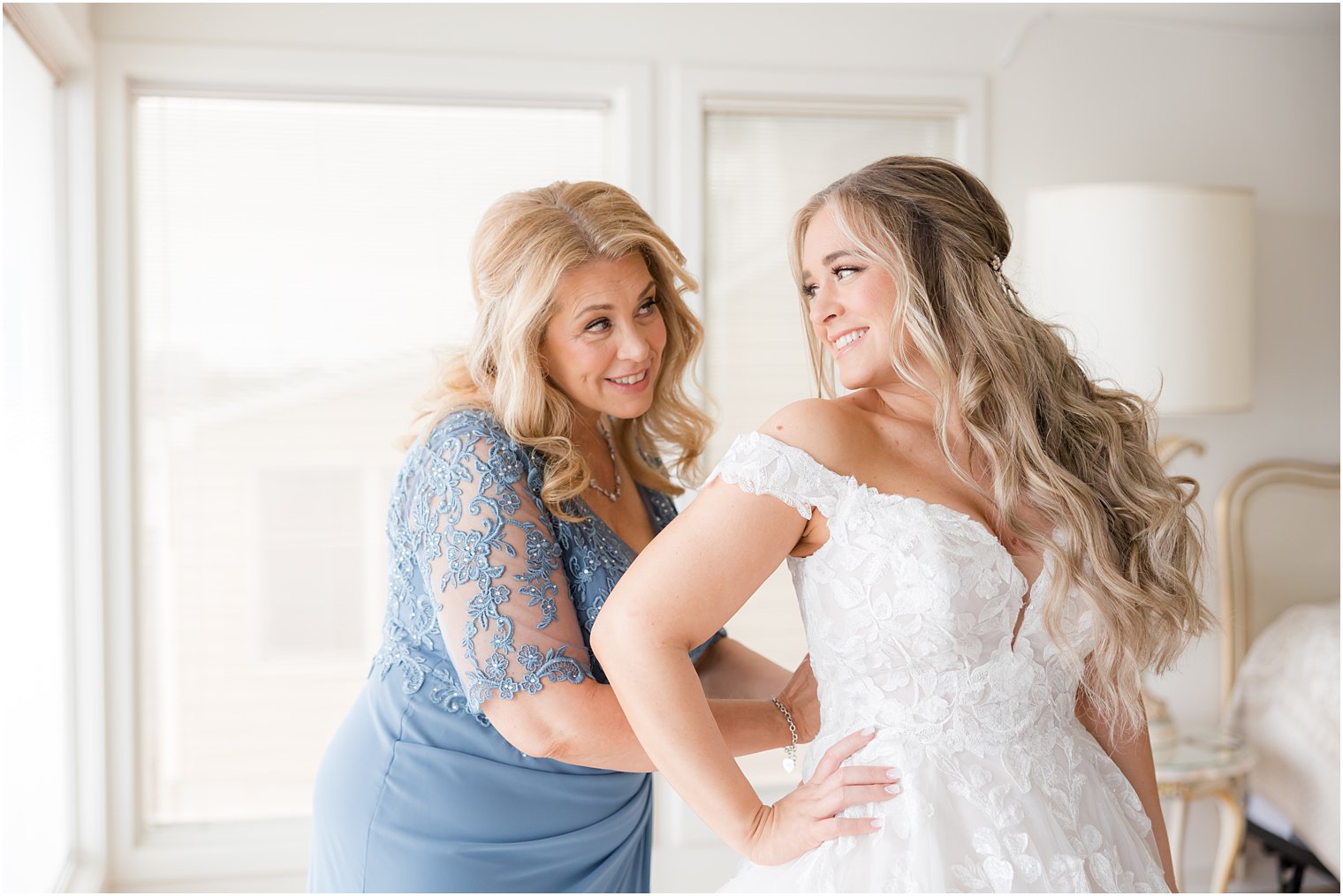 bride and mom smile while mom buttons up wedding dress at Point Pleasant NJ airbnb
