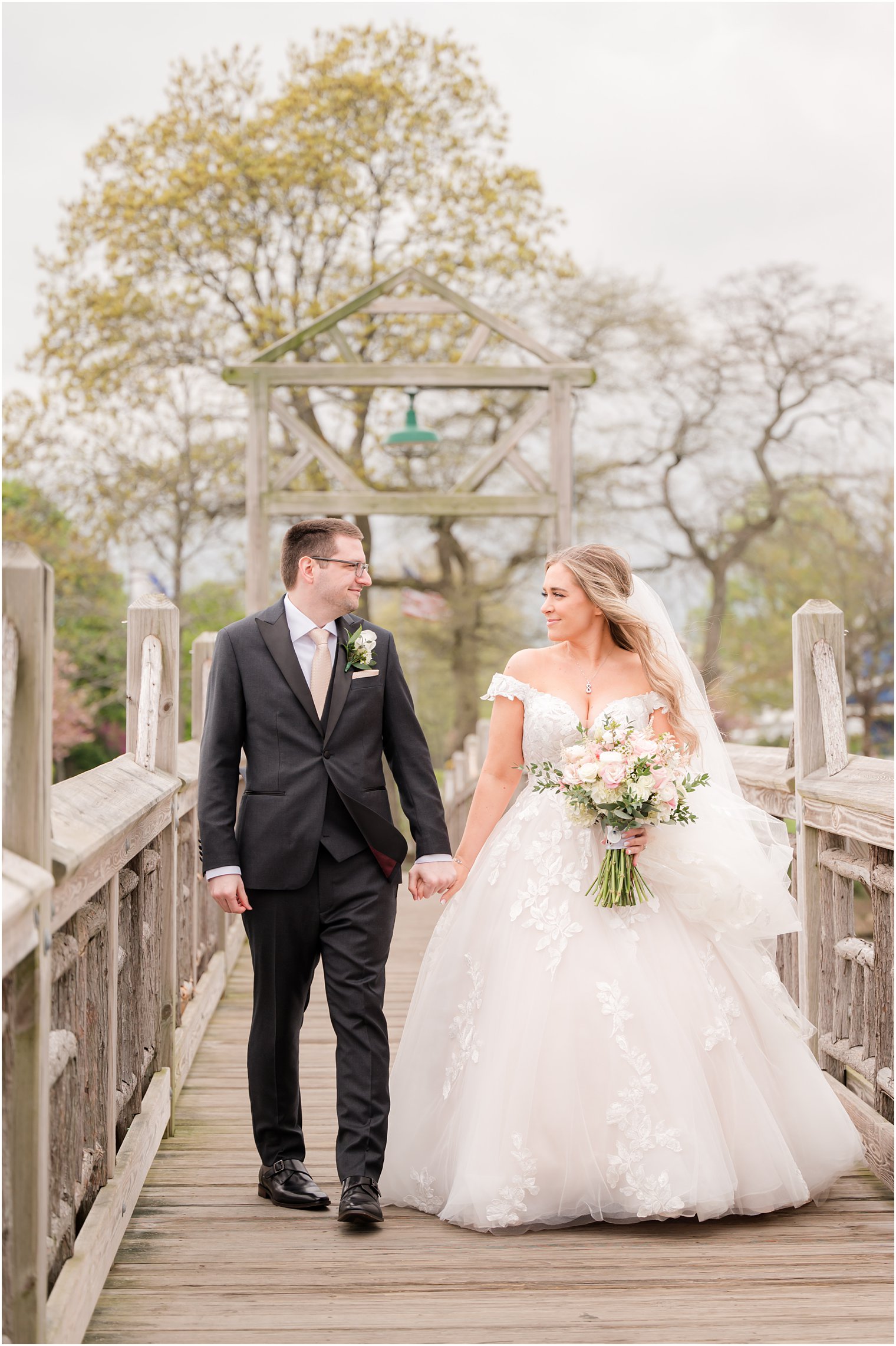 newlyweds hold hands walking on wooden bridge in Divine Park