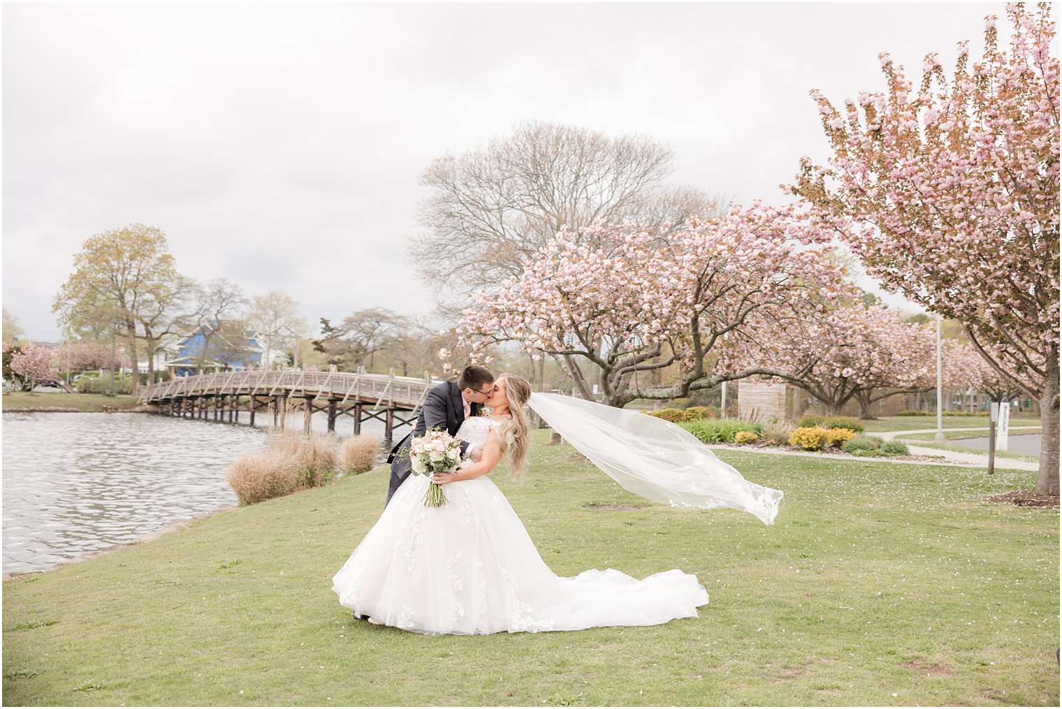 groom dips bride kissing her while veil floats behind them in front of cherry blossoms trees 