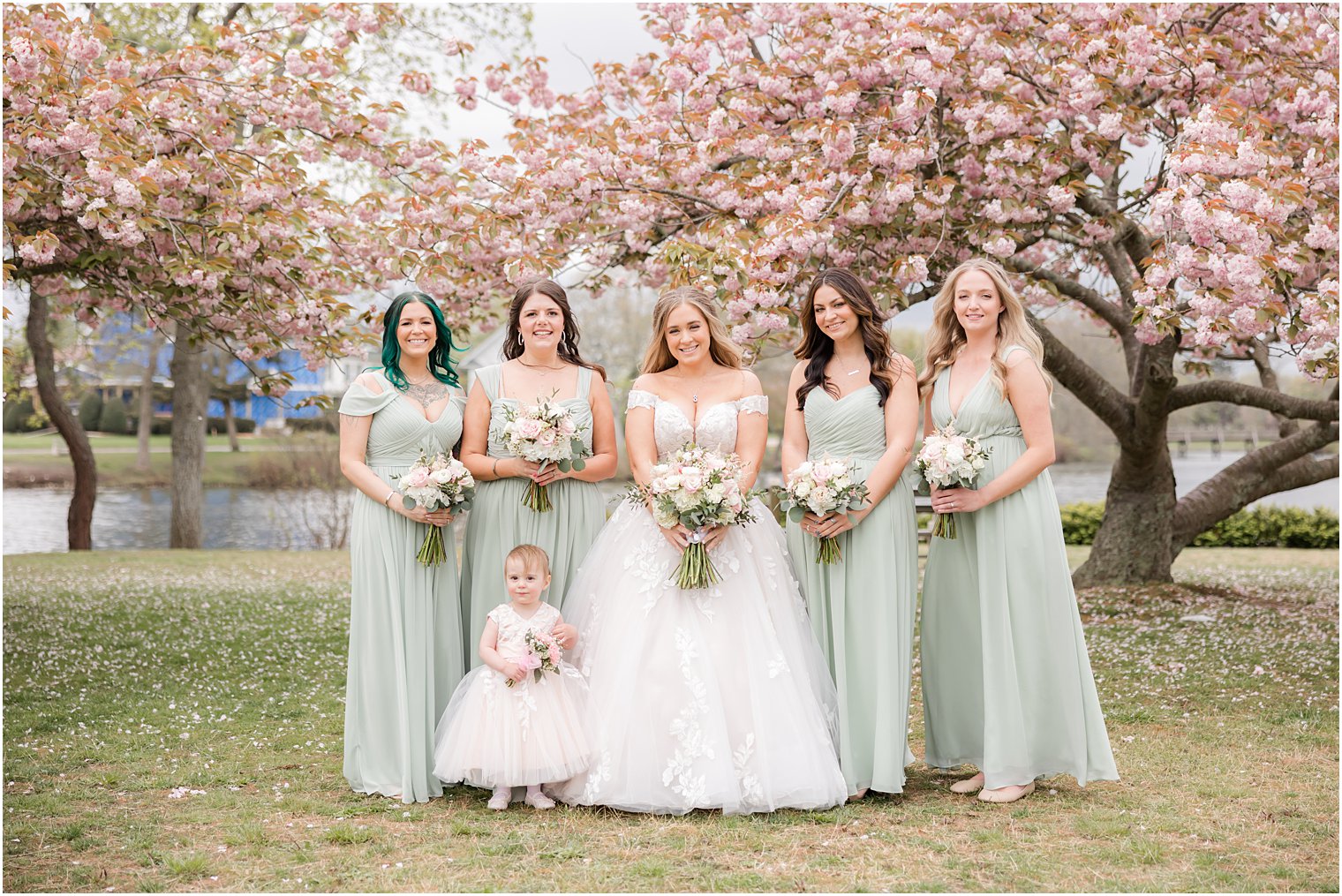 bride poses with bridesmaids in mint green gowns by cherry blossom trees