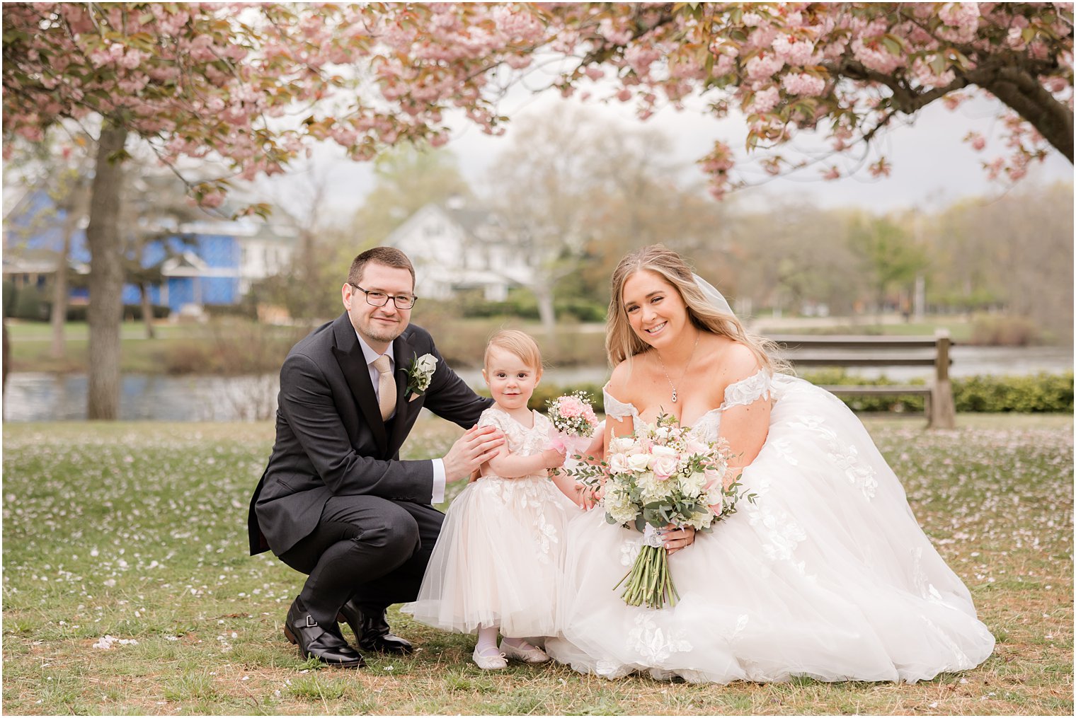 bride and groom kneel down with flower girl during spring wedding photos ub Divine Park in Spring Lake NJ