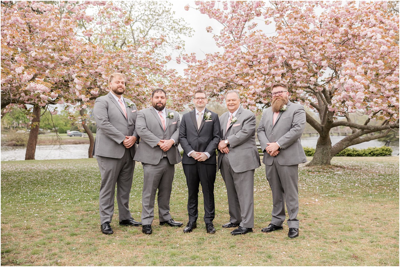 groom stands with groomsmen in grey suits in Divine Park in Spring Lake NJ