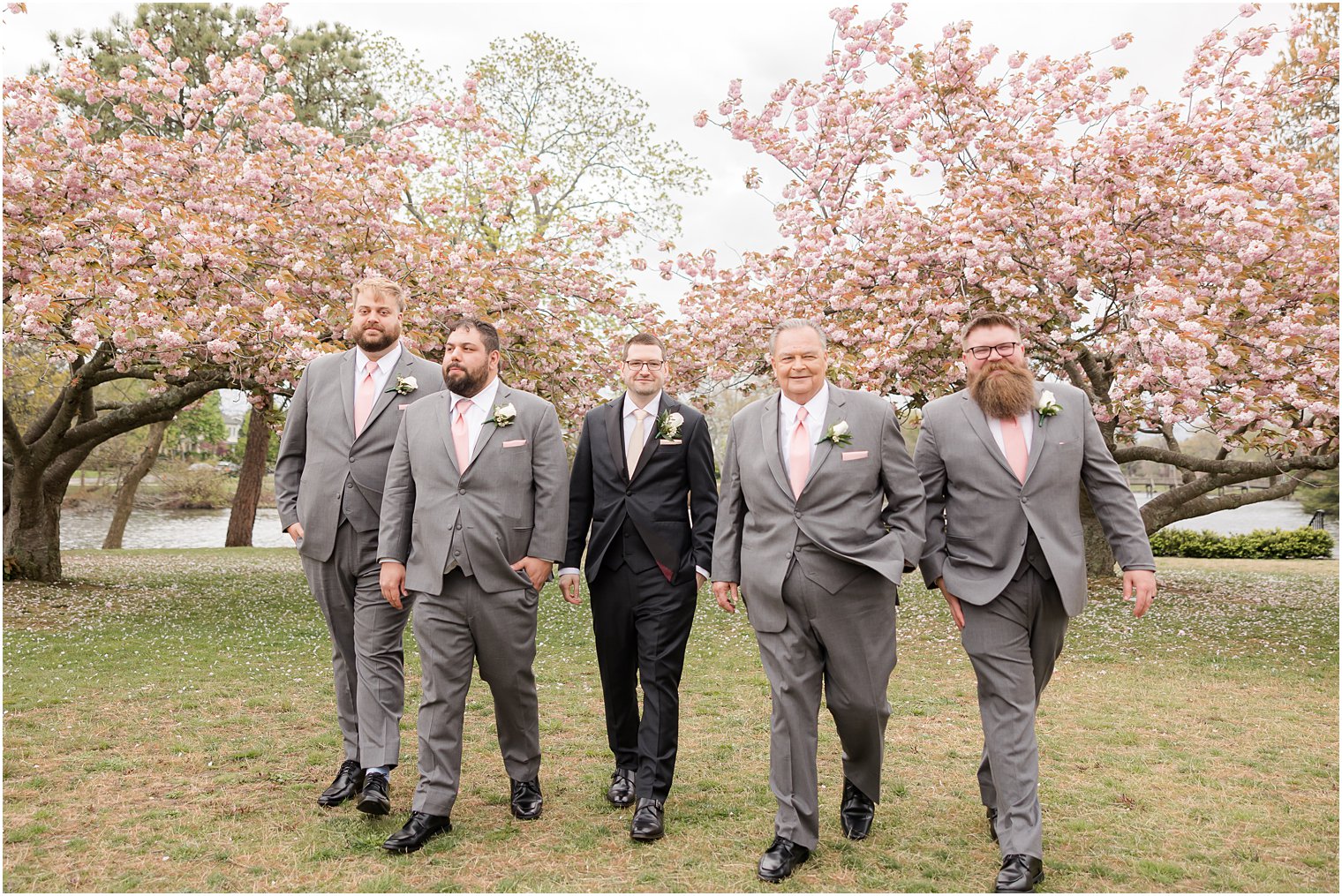 groom and groomsmen walk through trees at Divine Park in Spring Lake NJ