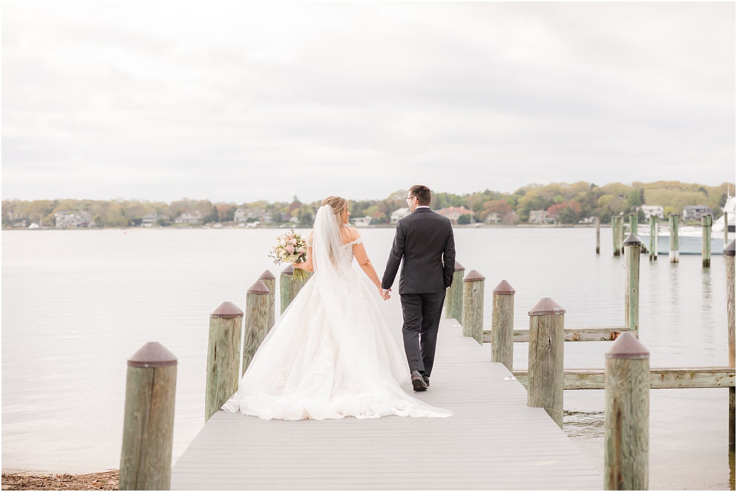 bride and groom hold hands walking down dock at Clark's Landing Yacht Club