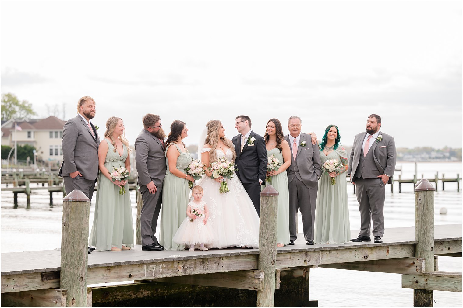 bride and groom smile together with wedding party around them on dock at Clark's Landing Yacht Club