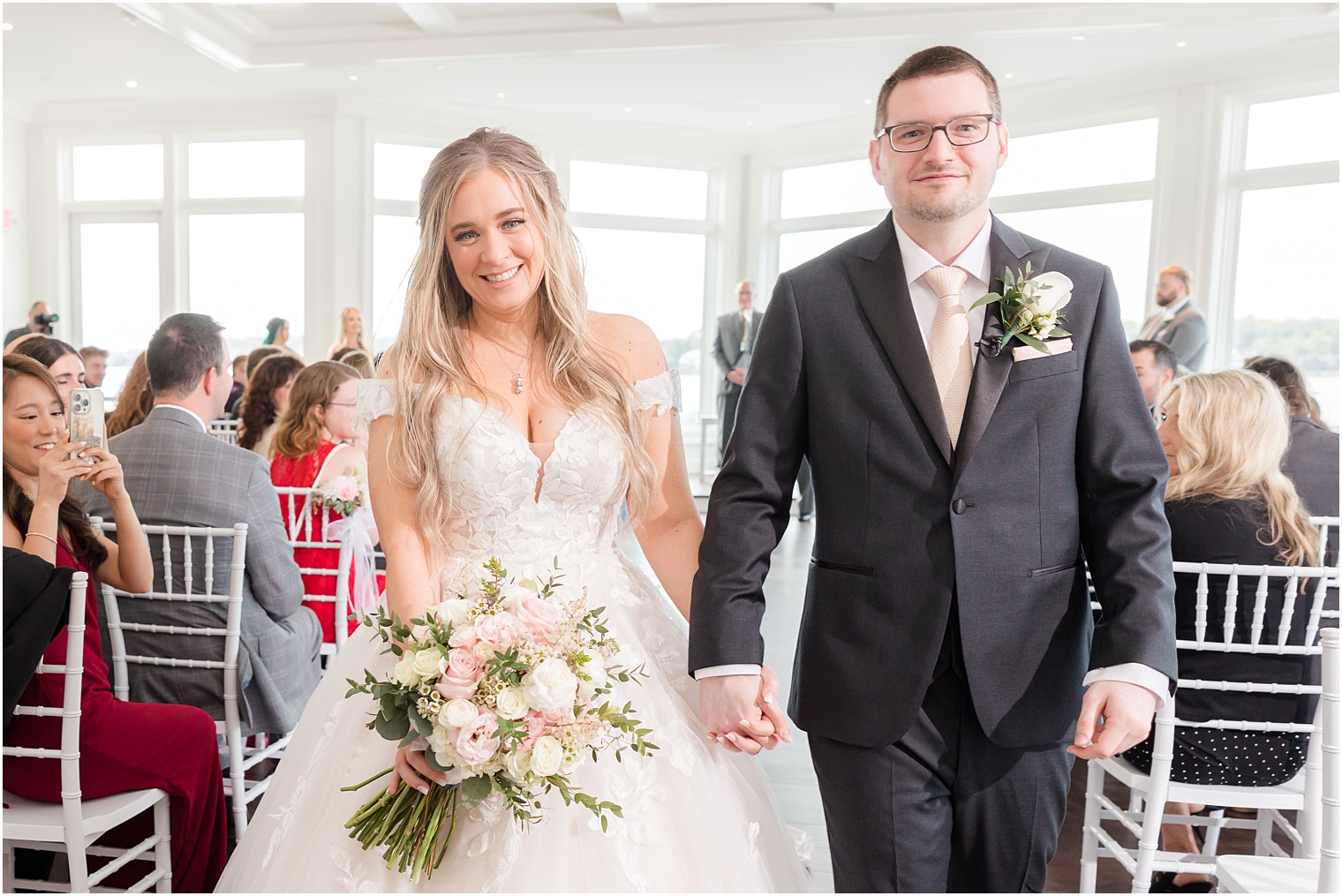 couple holds hands walking up aisle after ceremony 