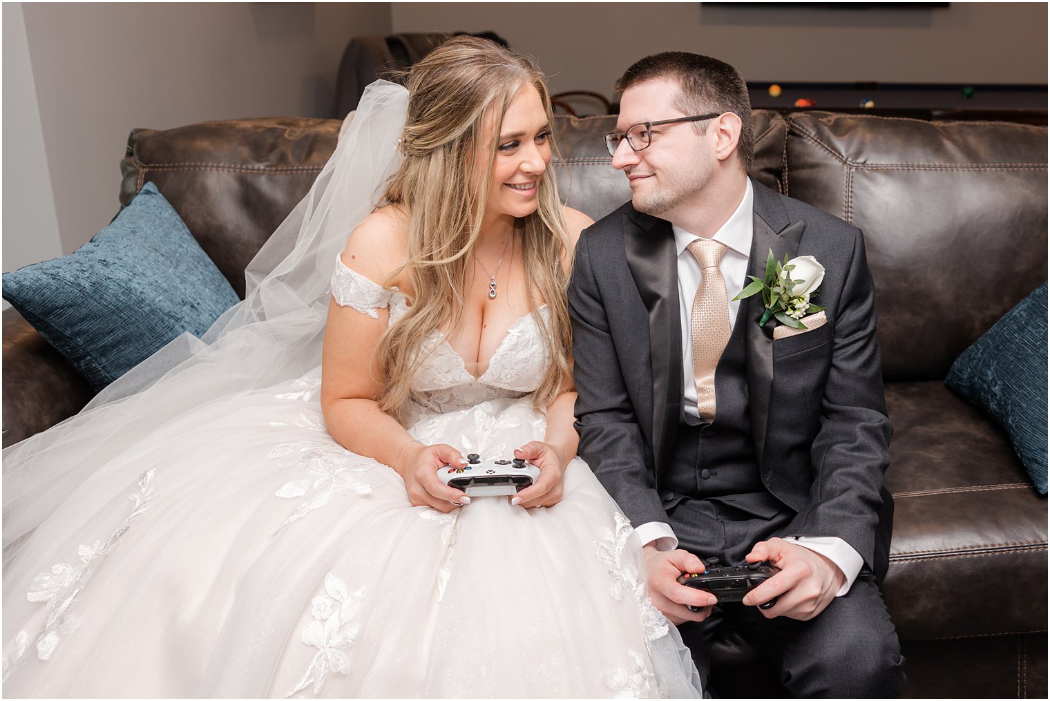 newlyweds sit on leather couch with gaming controllers