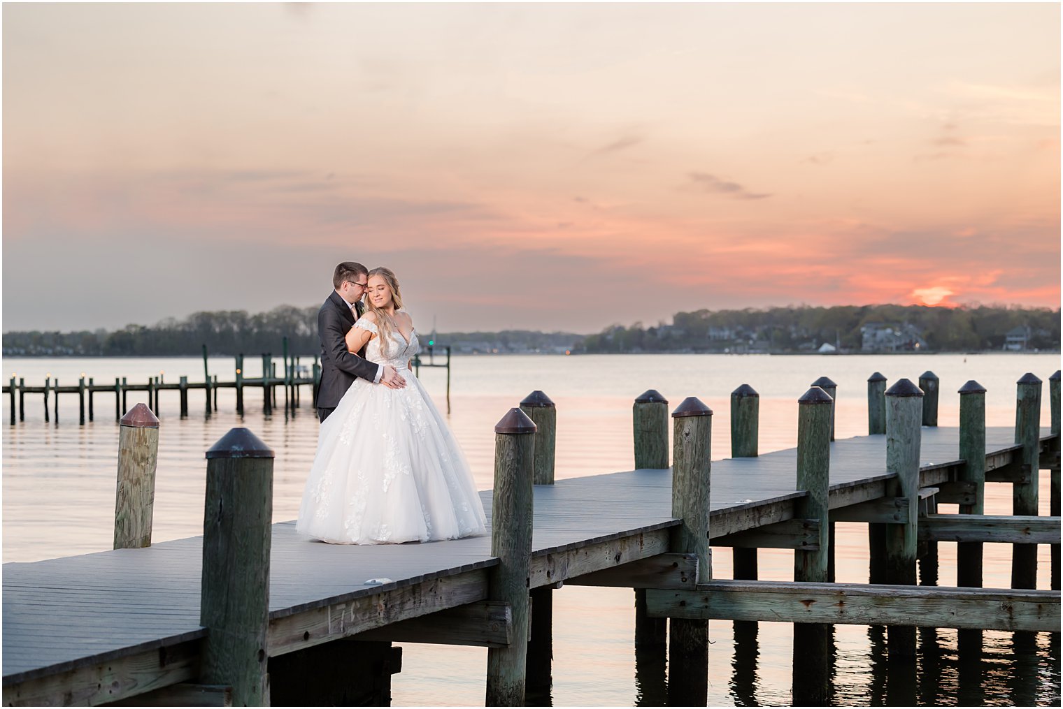 bride and groom hug on dock at sunset outside Clark's Landing Yacht Club