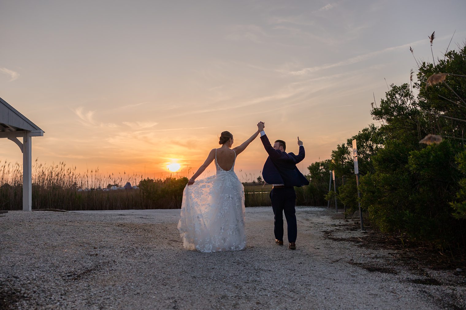 Couple holding hands, celebrating their wedding with the sunset of background at Bonnet Island Estate