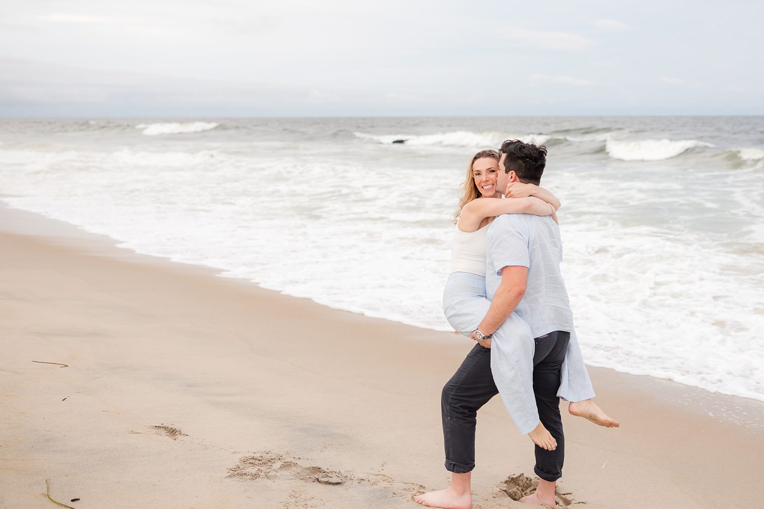 fiancé holding up to his bride next to the beach