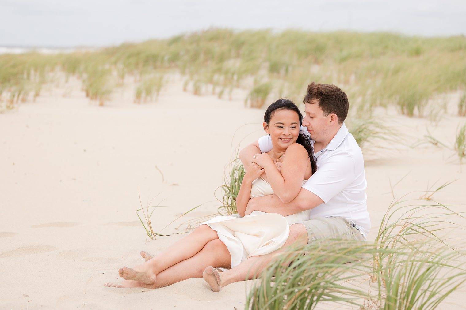 bride and fiancé sitting in the sand 
