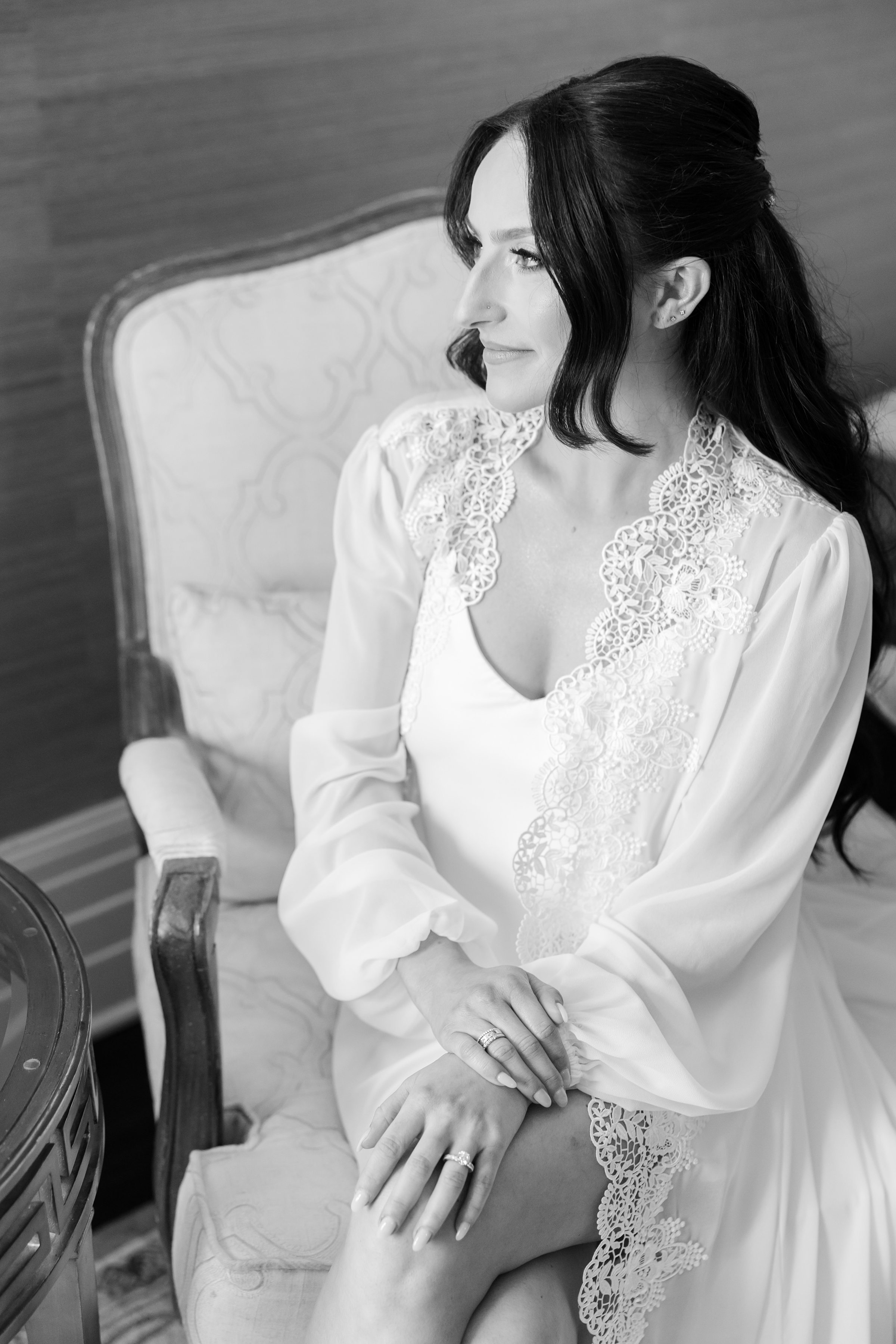 Bride wearing a white lace robe while looking to the side with curled black hair