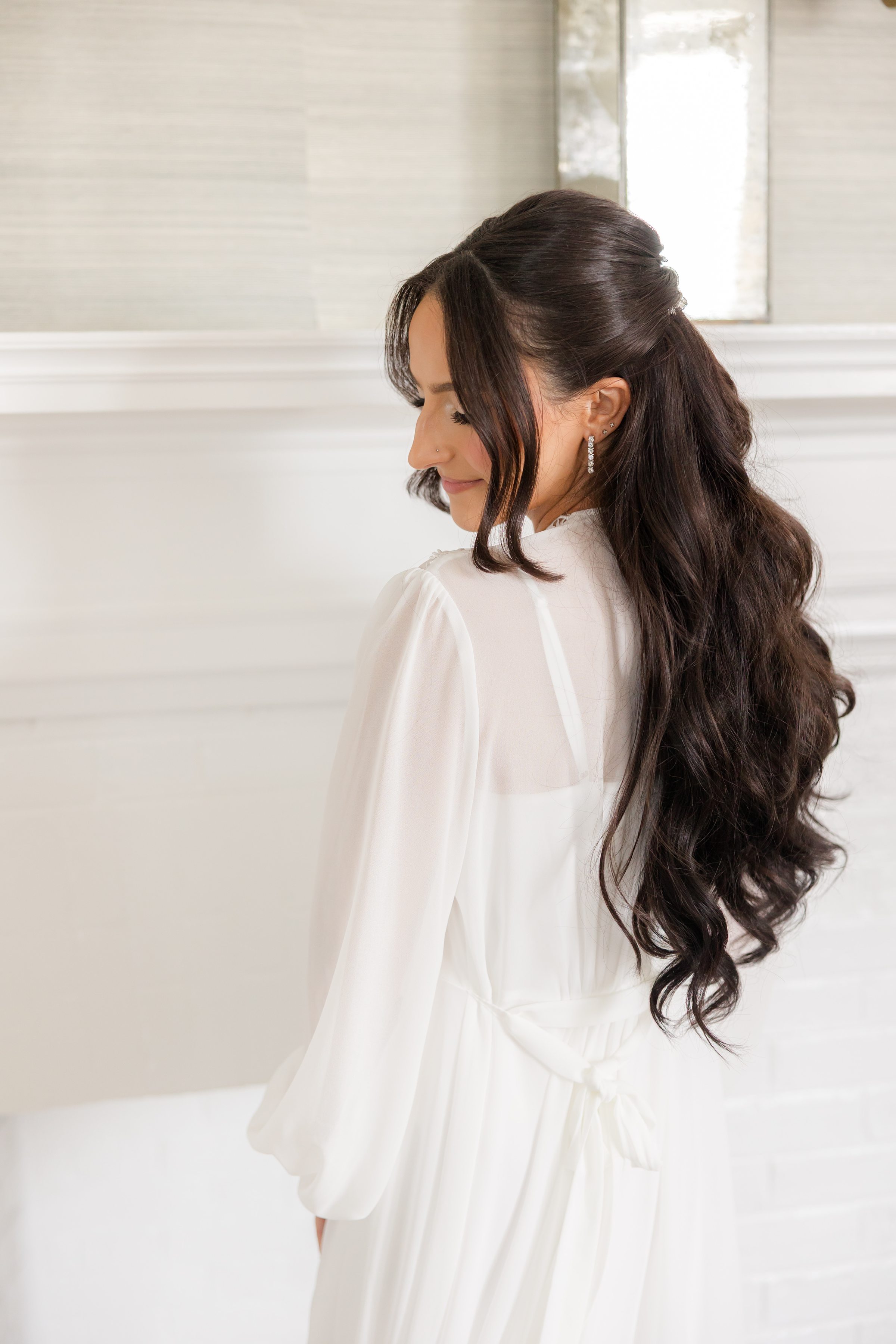 Bride wearing a white lace robe while smiling, curled black hair with makeup
