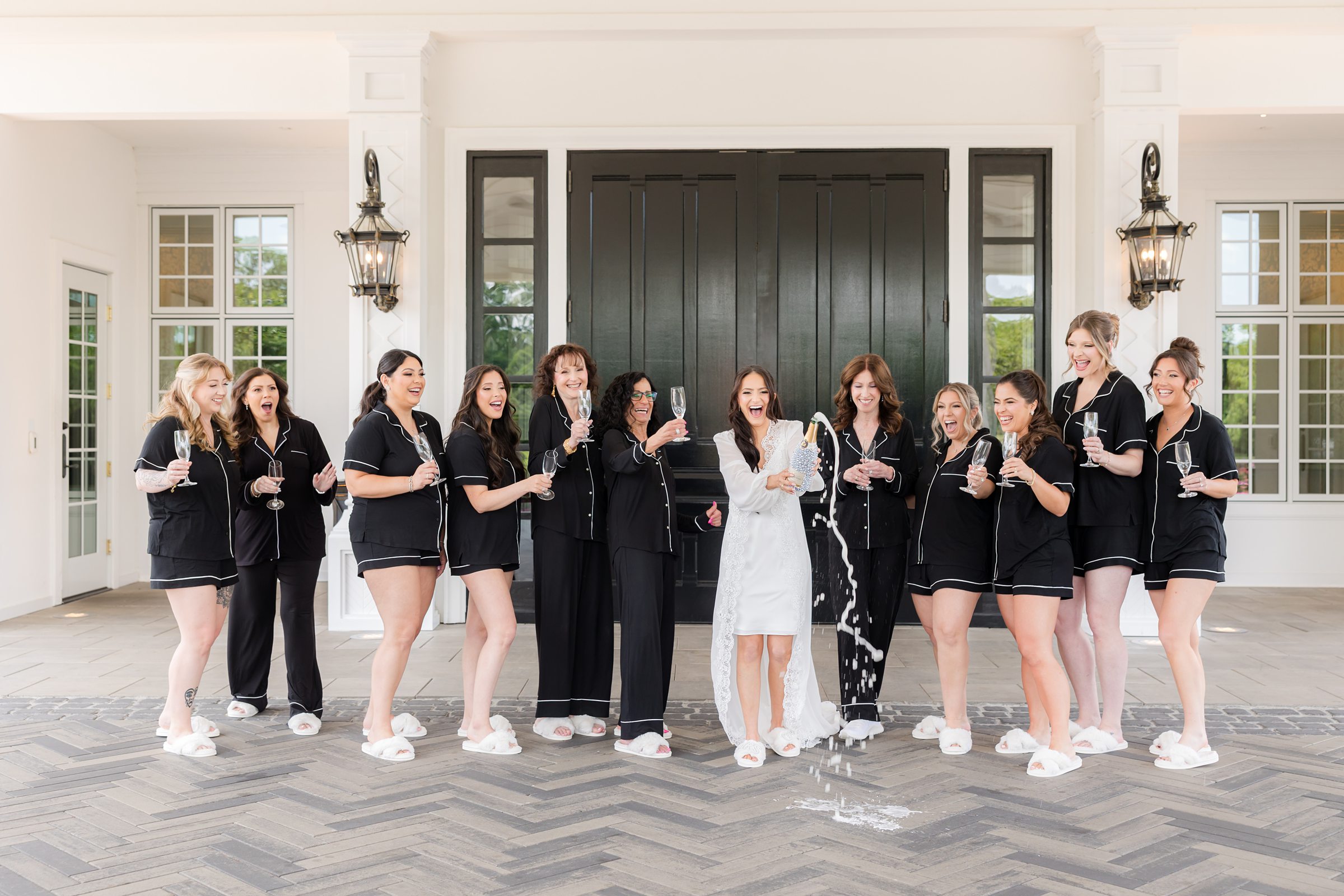 Bride opening the bottle of champagne with bridesmaids holding their glass