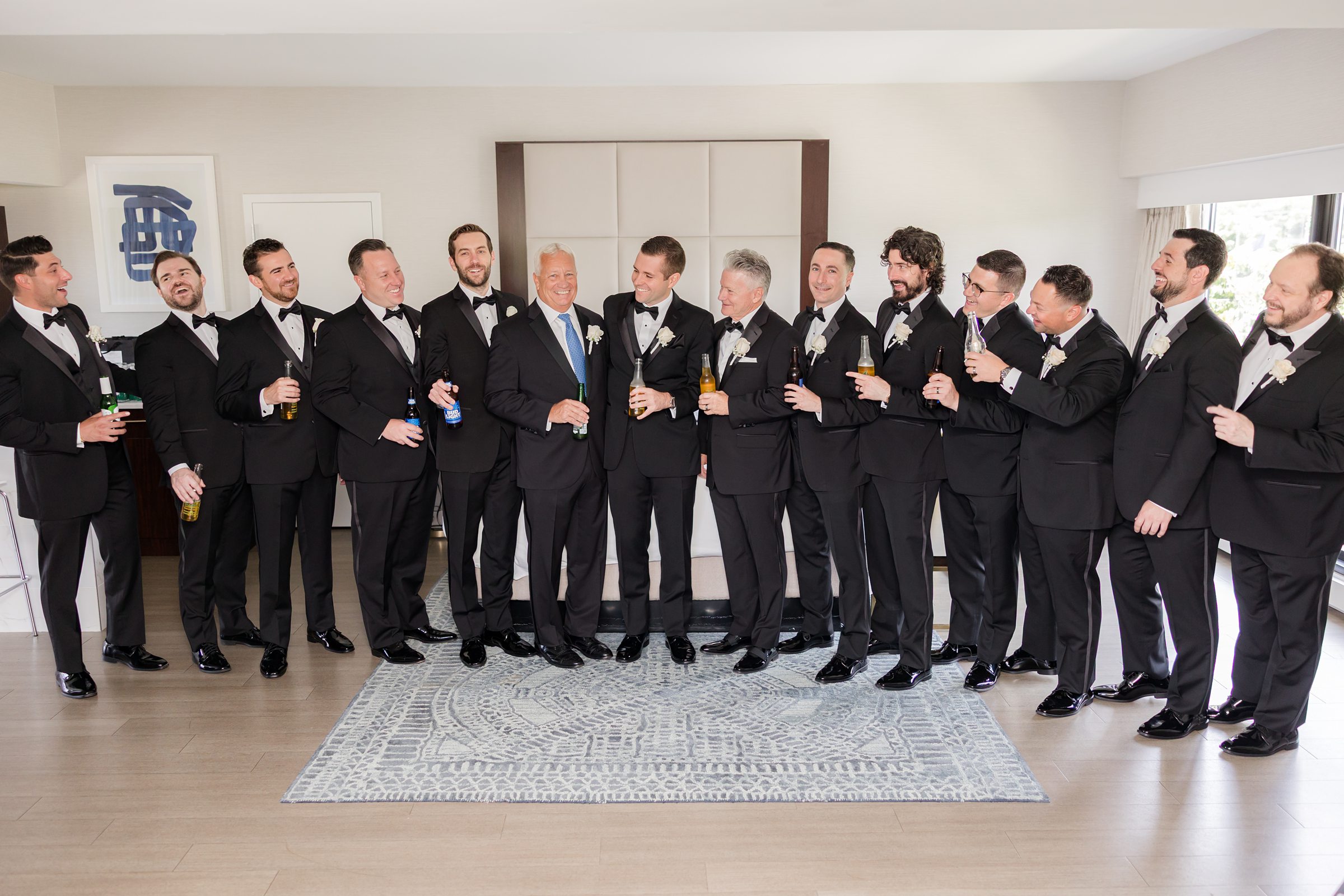 Picture of groom with groomsmen wearing black tuxedo, holding a bottle of drinks