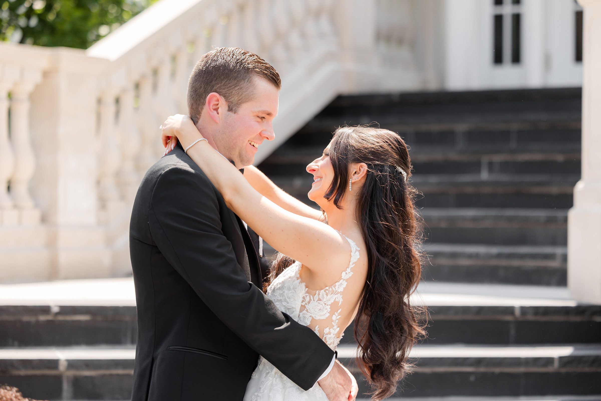 Bride is wrapping her arms around groom's neck, while smiling at each other